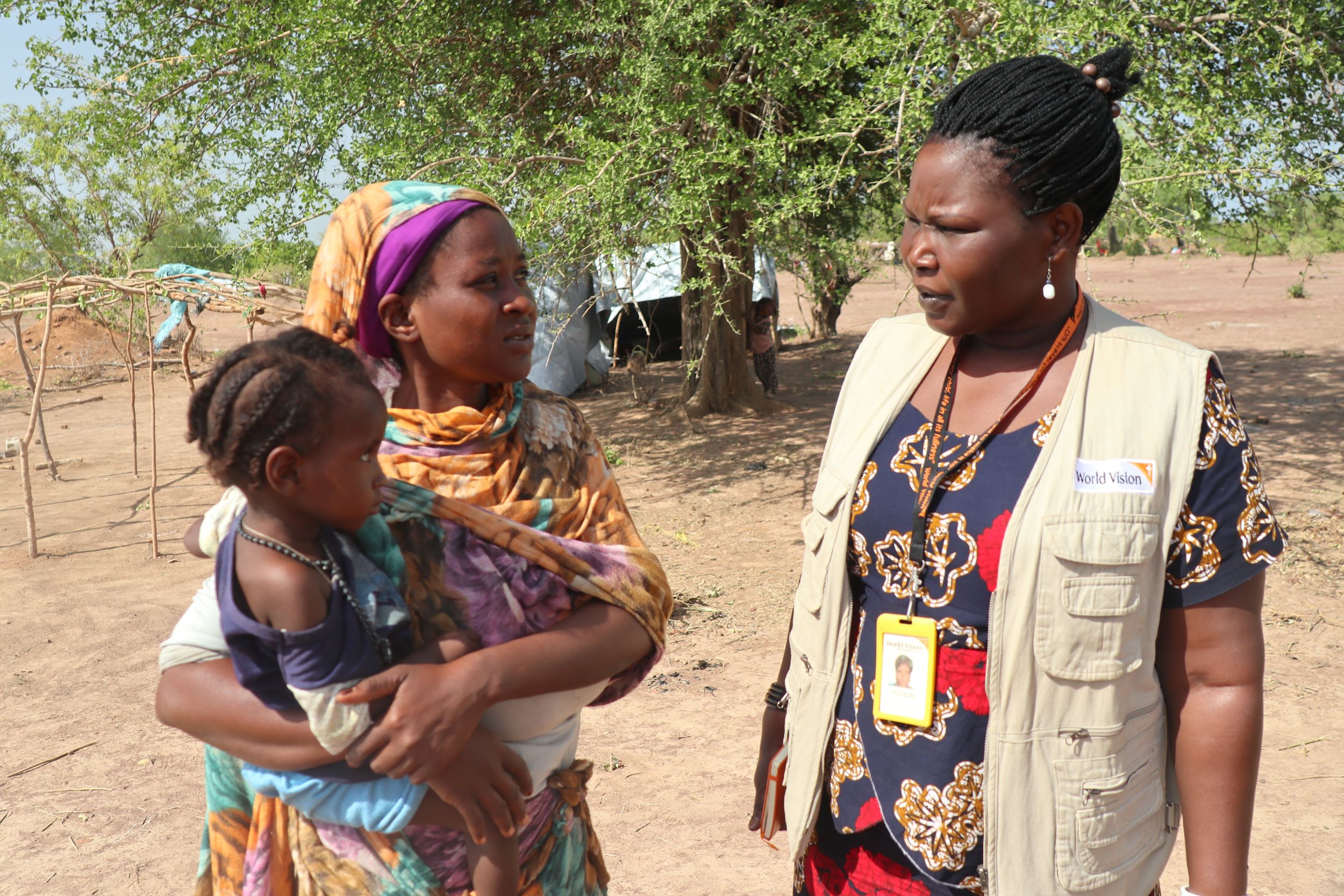 A refugee from Sudan holds her young child while talking to a World Vision staff member