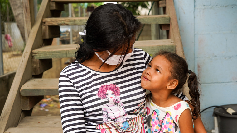 Girl sits on steps and looks up at a woman wearing a mask