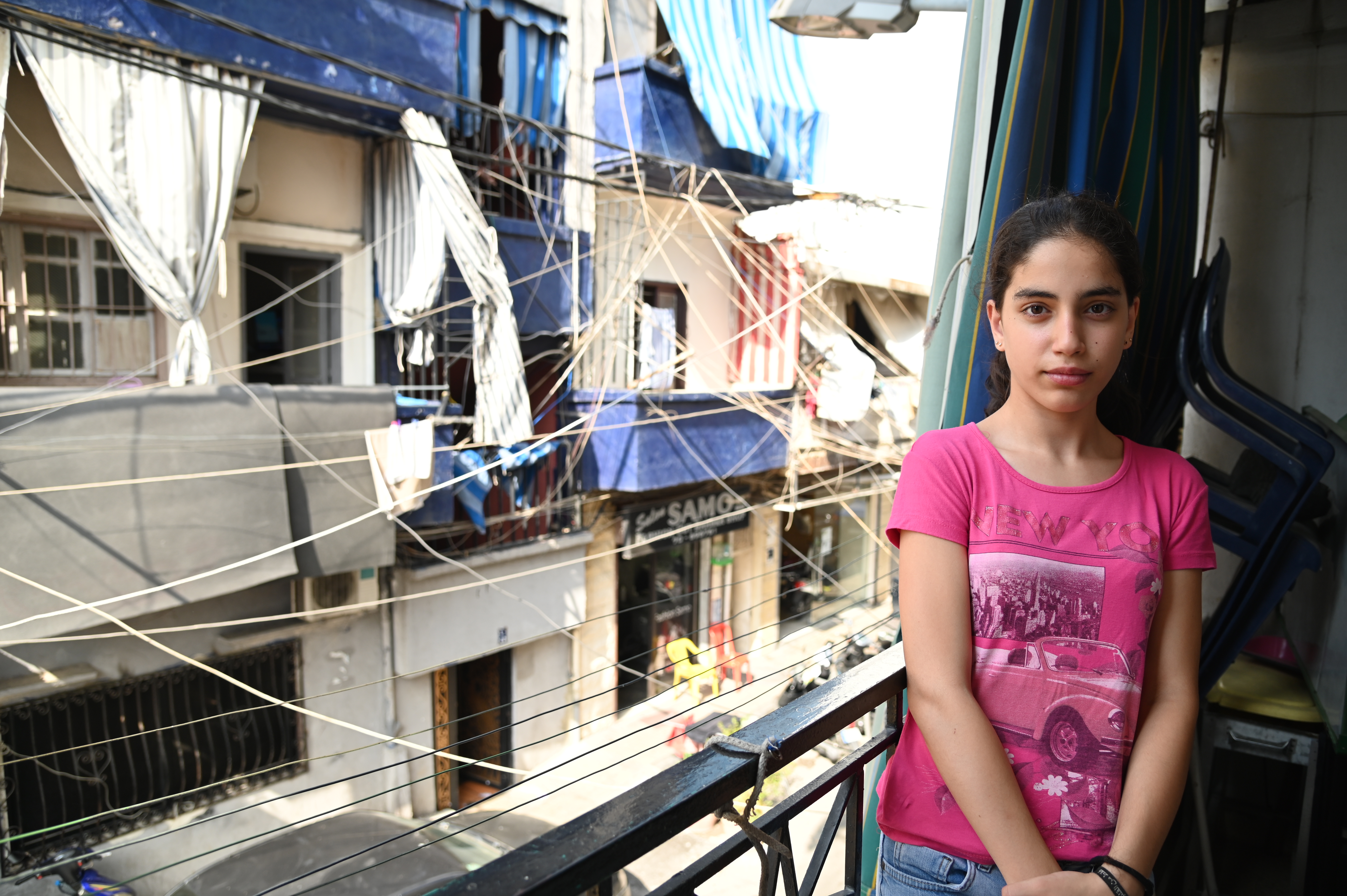 Girl in Lebanon stands next to a window in her home that was affected by the Beirut explosion