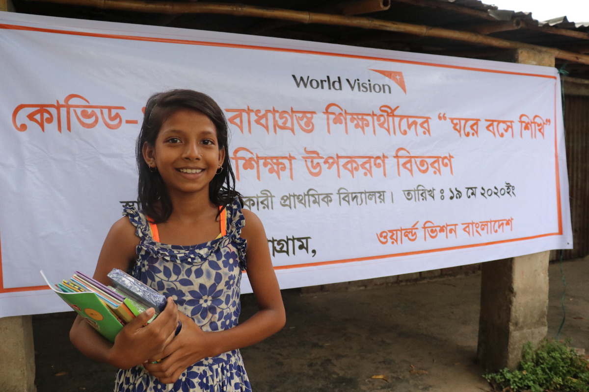 A girl holding books in front of a World Vision sign