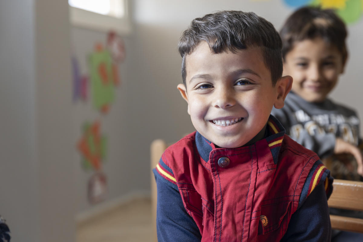 Syrian child smiles in a classroom in Lebanon, a smiling child sitting behind him