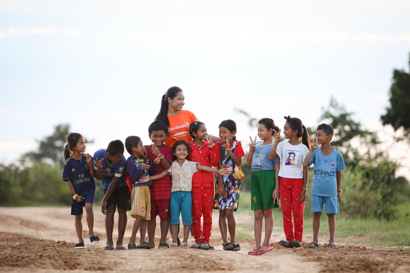 Cambodian children smiling with World Vision staff member in a field