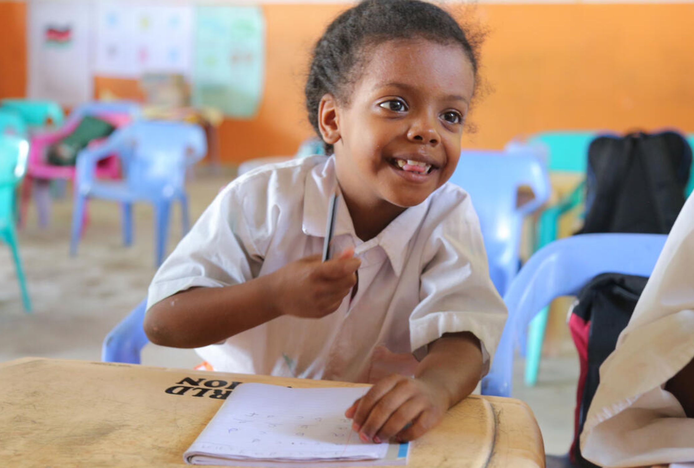 Kenyan six-year-old girl sat at a desk with a cheeky smile