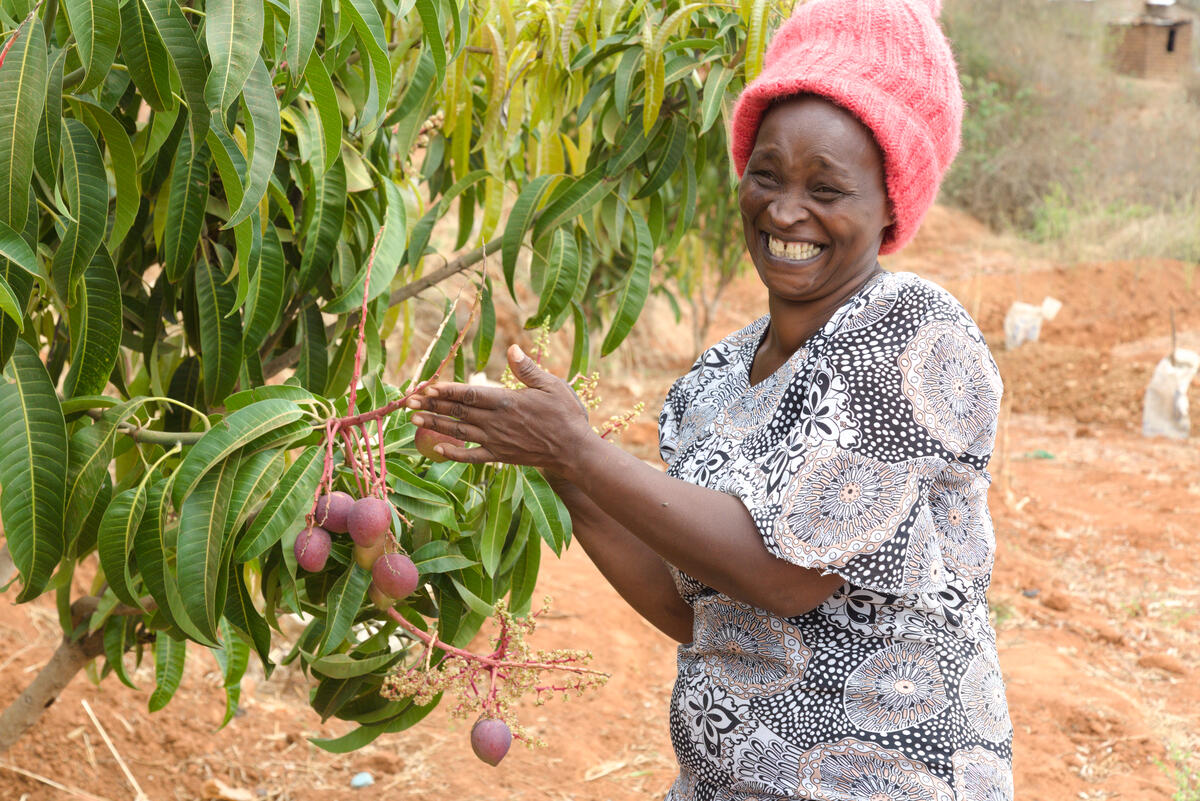 A woman smiles broadly as she shows the fruit growing on her trees