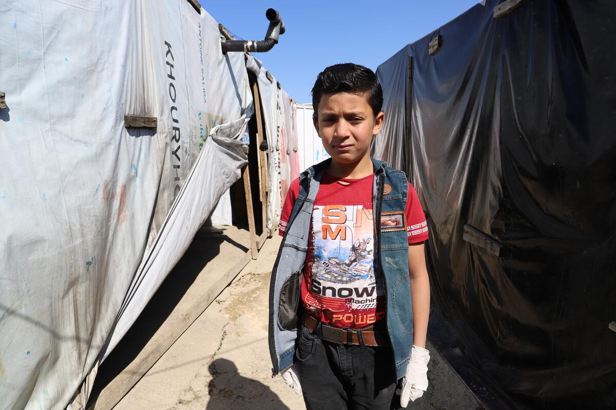 Syrian boy stands in a gap between tents in a refugee camp in Lebanon