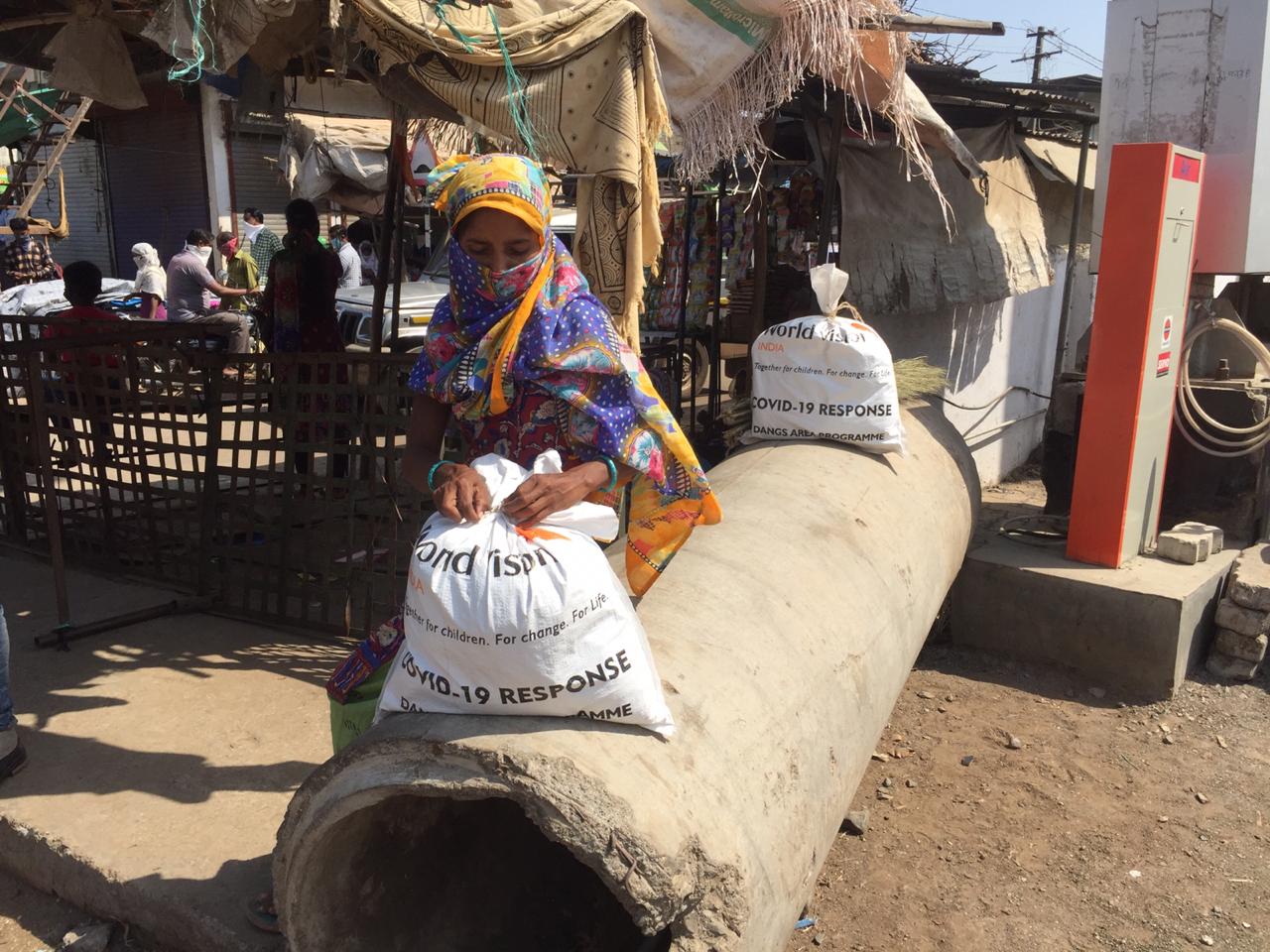 Woman in India sits outside holding a bag of food rations
