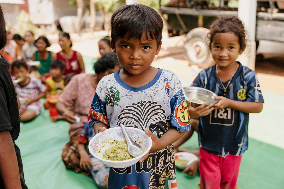 A young boy holds a bowl of food, looking to camera. Cambodia