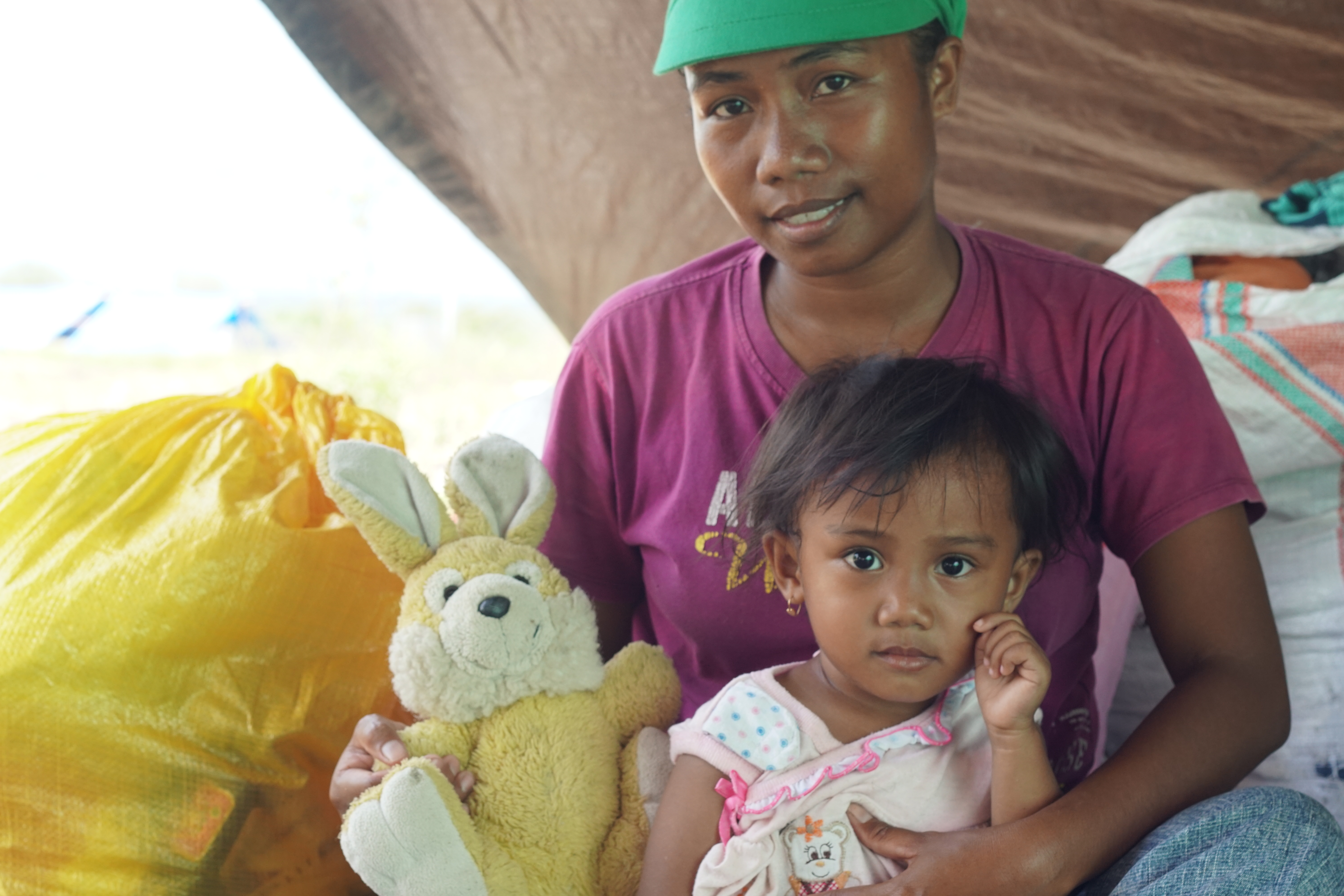 Indonesian person holds a child and a teddy sitting in an emergency tent