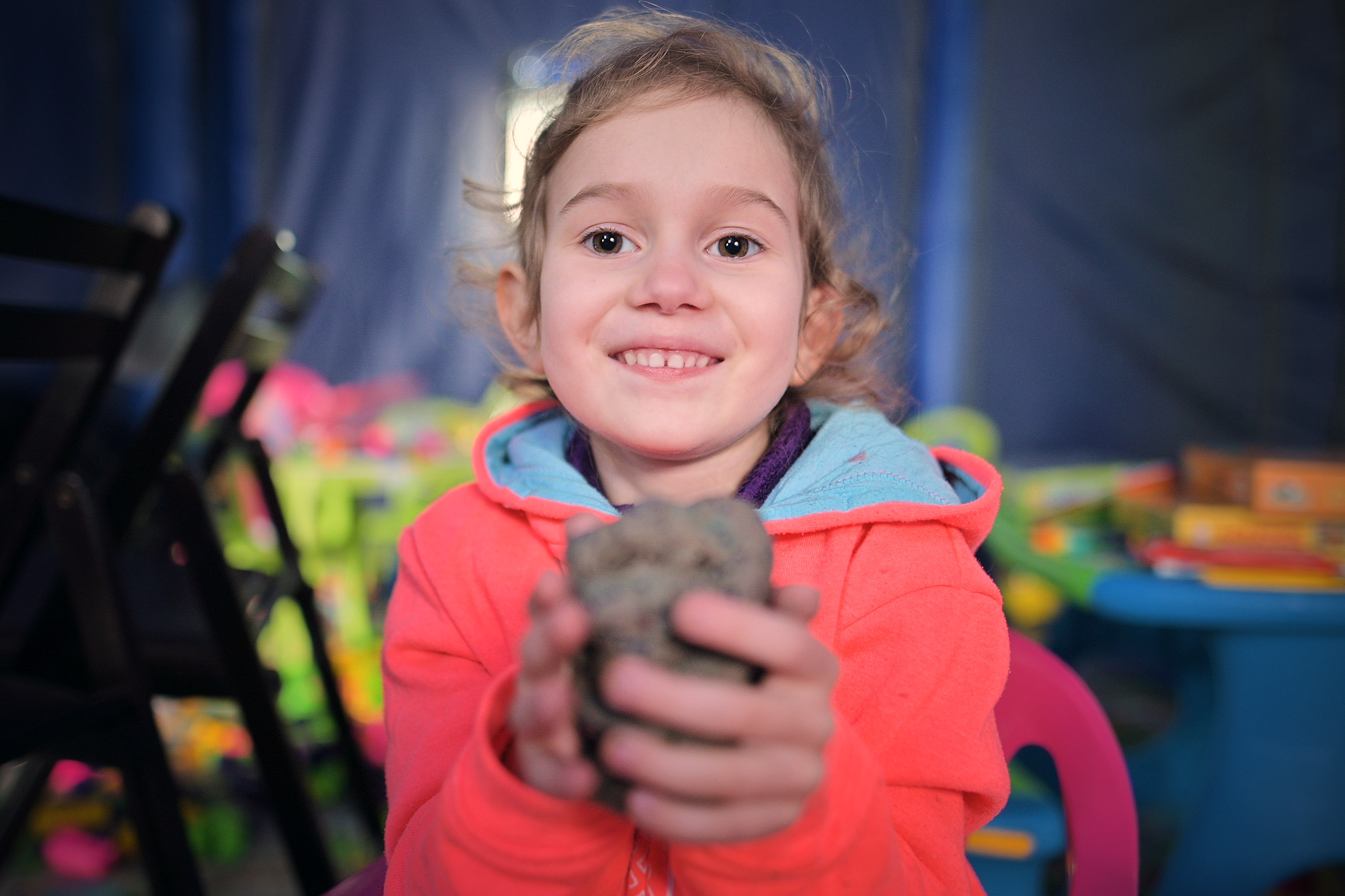A young girl smiling and holding a lump of clay to the camera