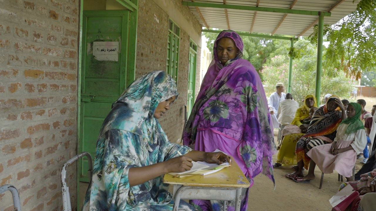 Two ladies at a table with others waiting to be seen be medical professionals in Sudan