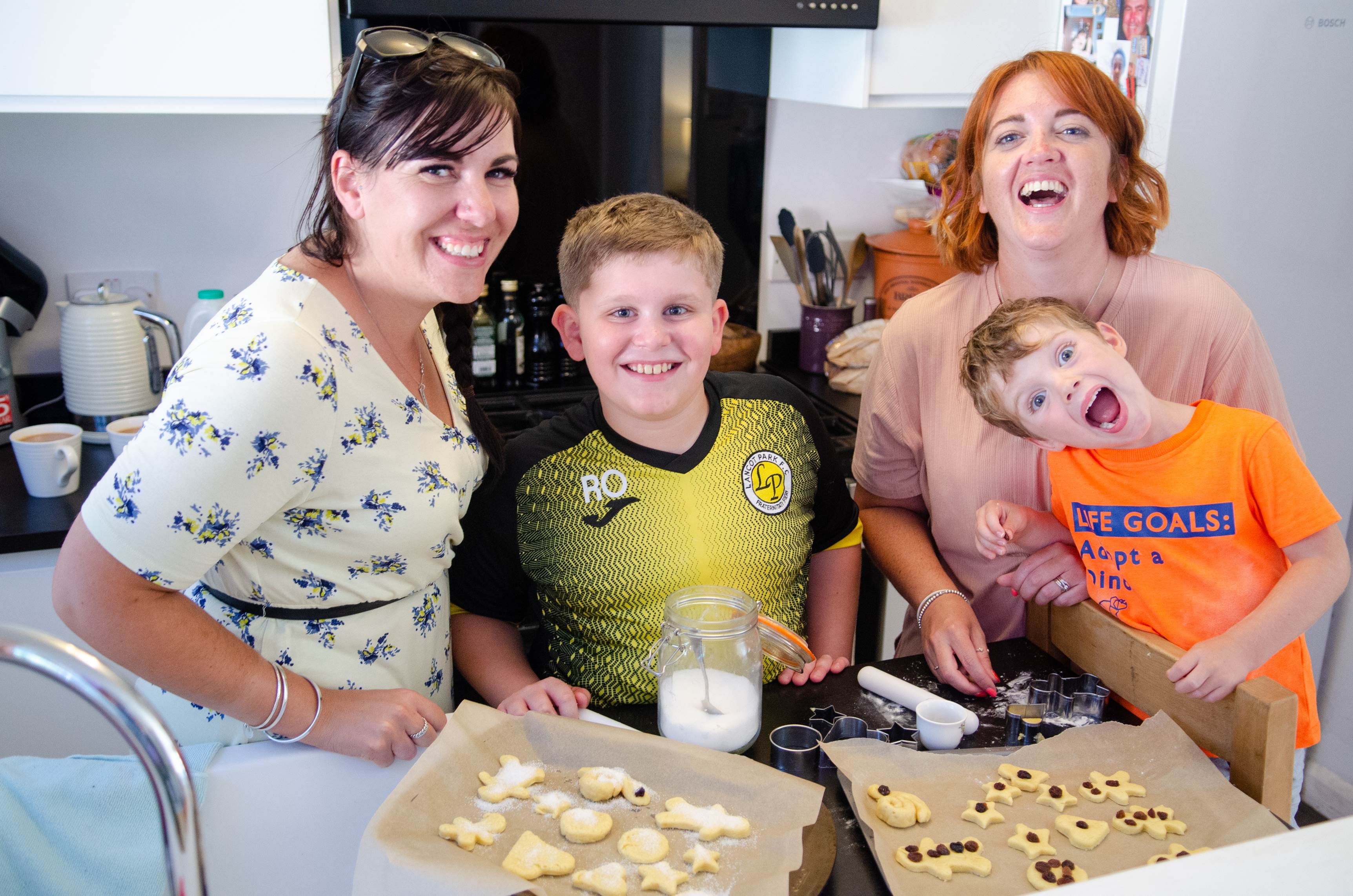 Two women with two boys all smiling to camera with a tray of biscuits in front of them while standing in a kitchen
