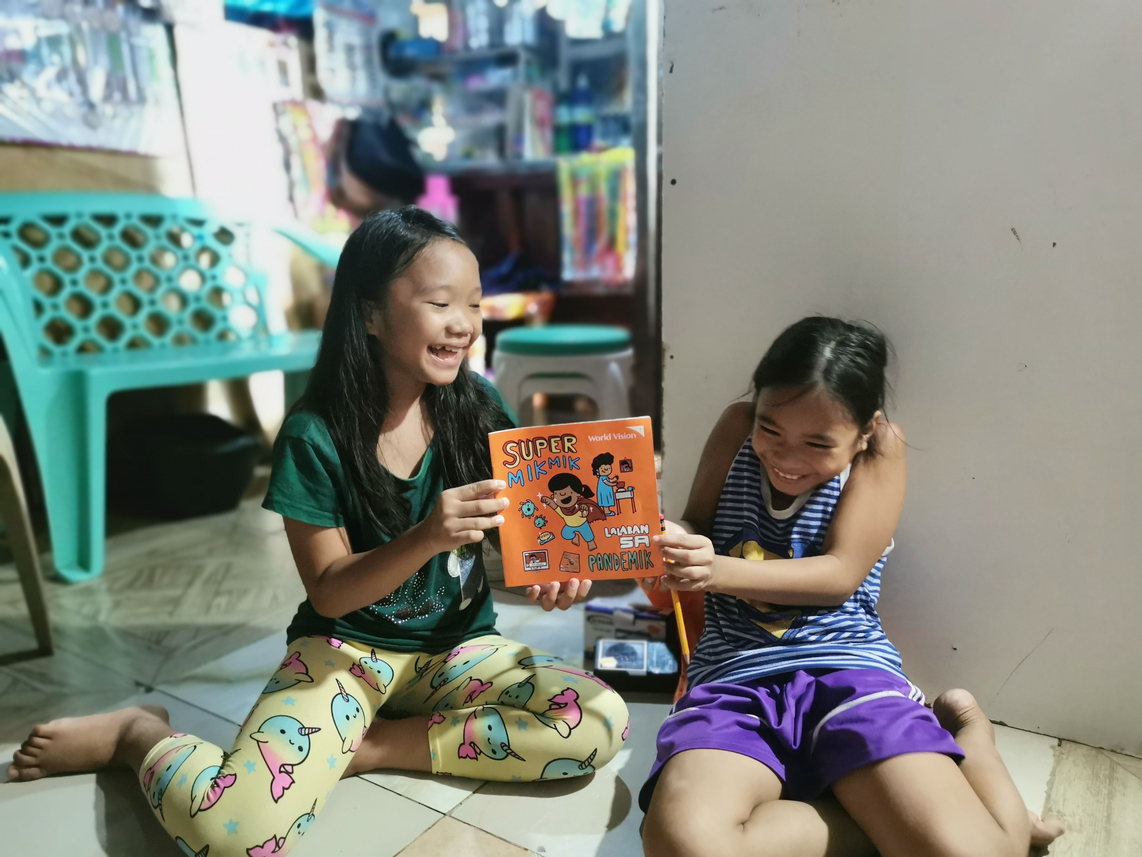 Two girls giggle as they hold a child protection magazine in the Philippines