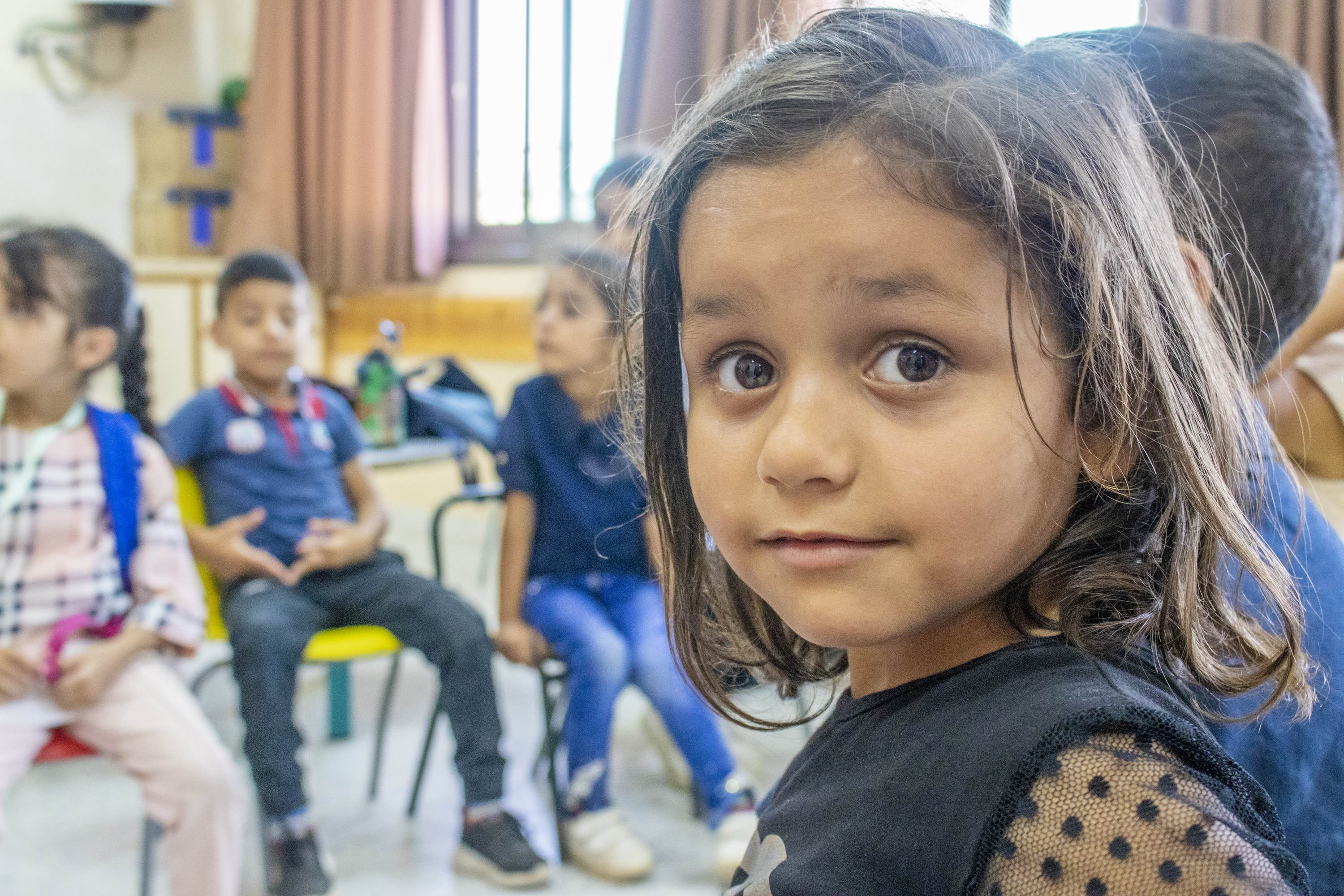Girl in Gaza looks around her shoulder as she sits in a classroom with other children