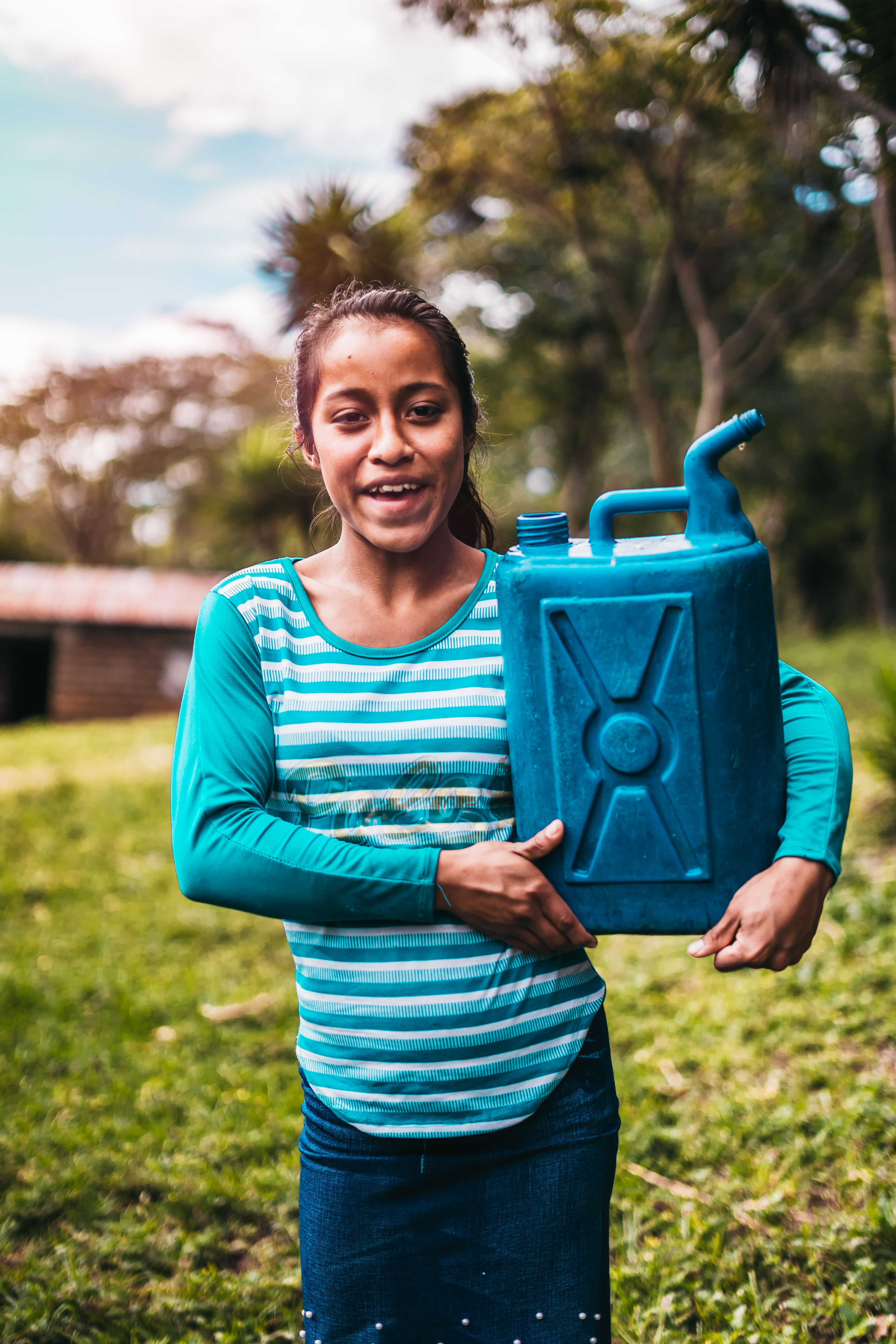 Teenage girl outside smiling as she holds her blue watering can
