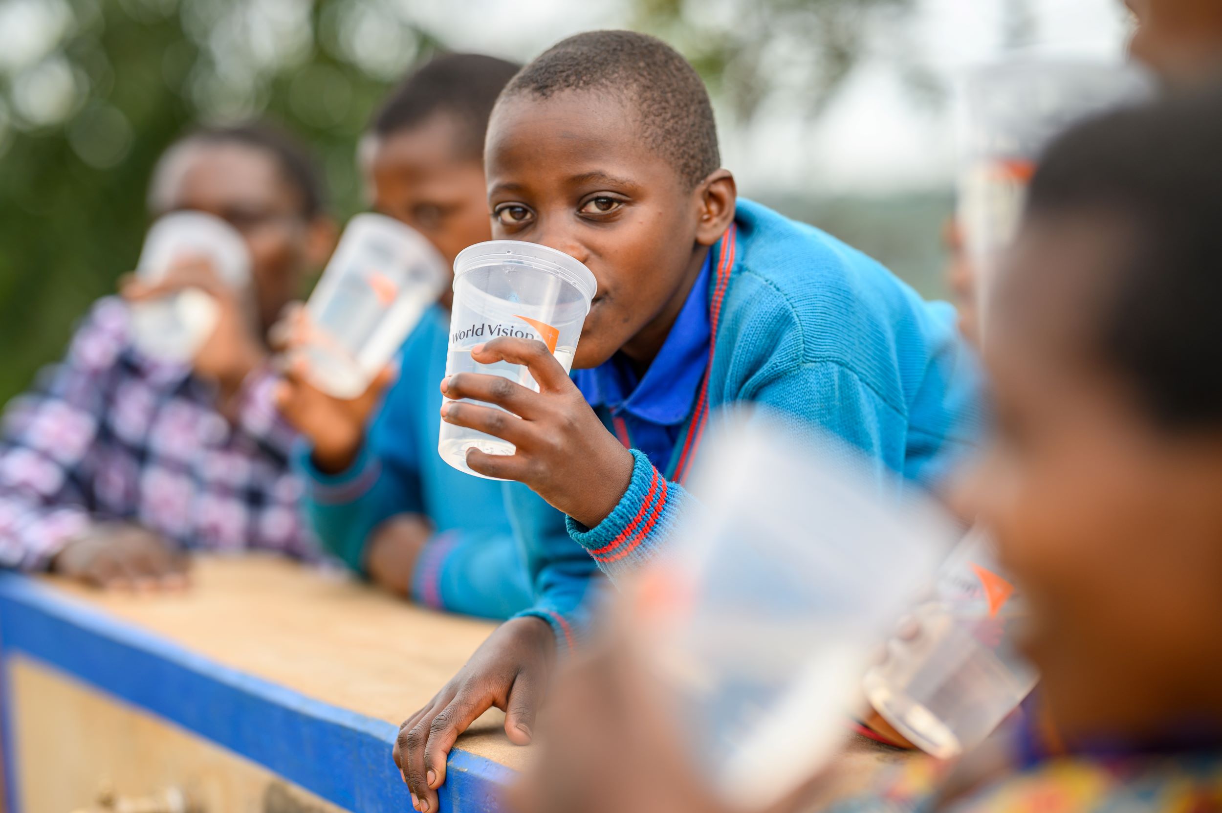 Girl wearing bright blue jumper, drinking clean water from a clear plastic cup