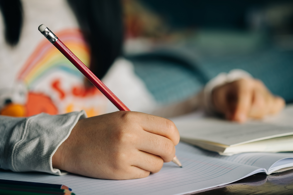 A child writing to their pen pal with paper and pencil