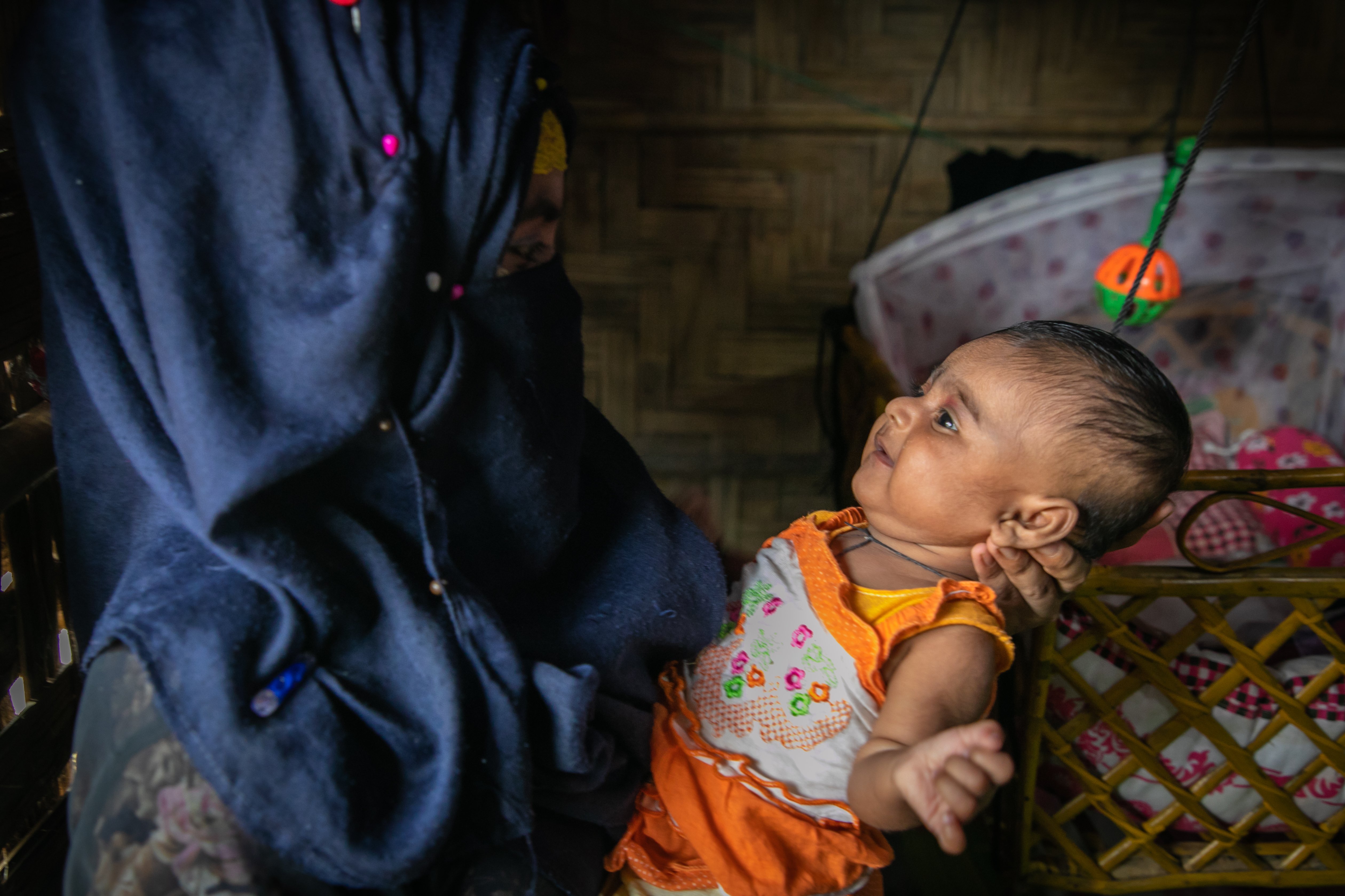 Girl in Bangladesh, whose face is covered, holds her baby in a Rohingya refugee camp