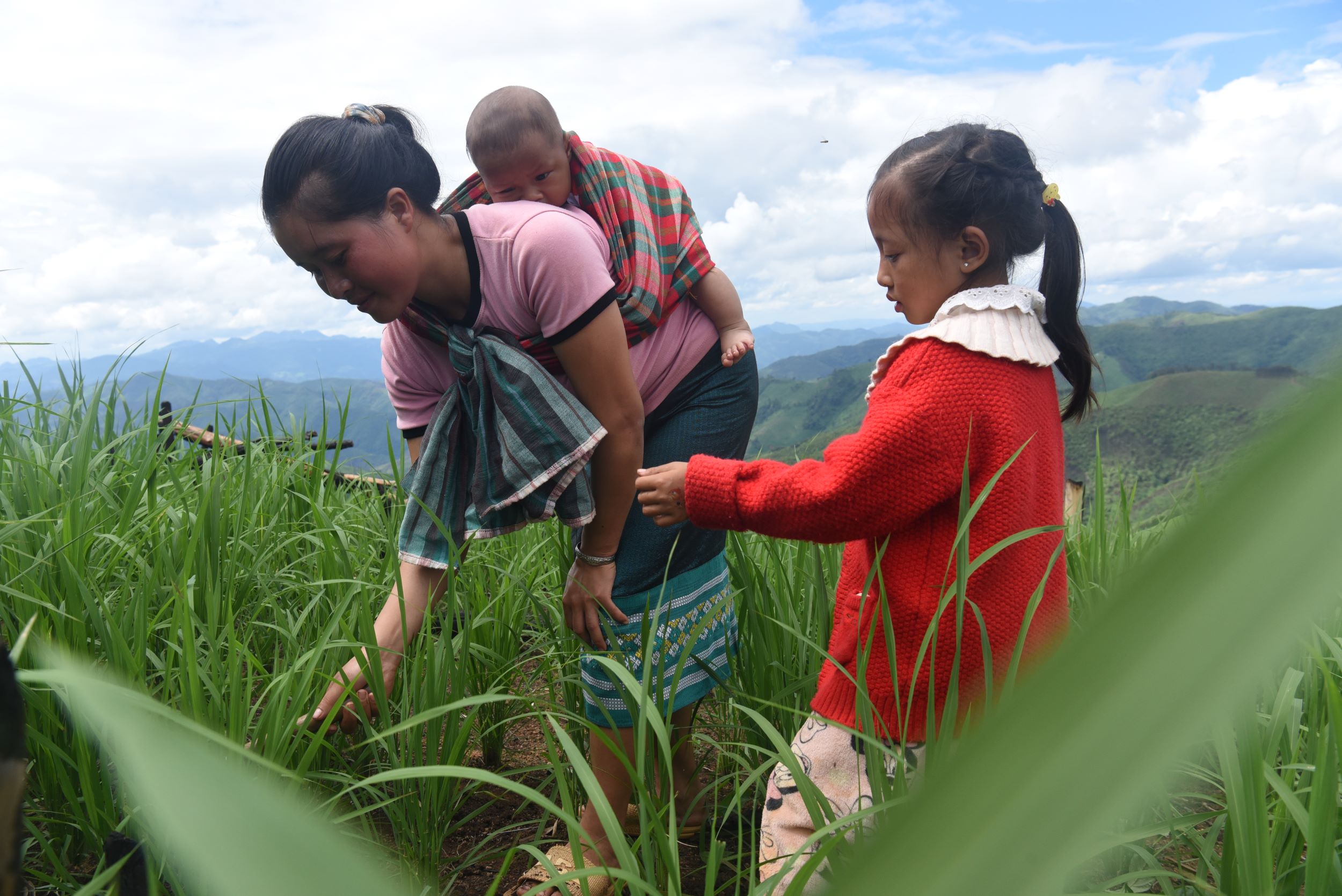 A woman tending to crops with help from her daughter while carrying a baby on her back