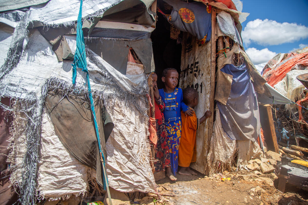 Three Somali children looking out the door of their temporary shelter made of tarpaulin