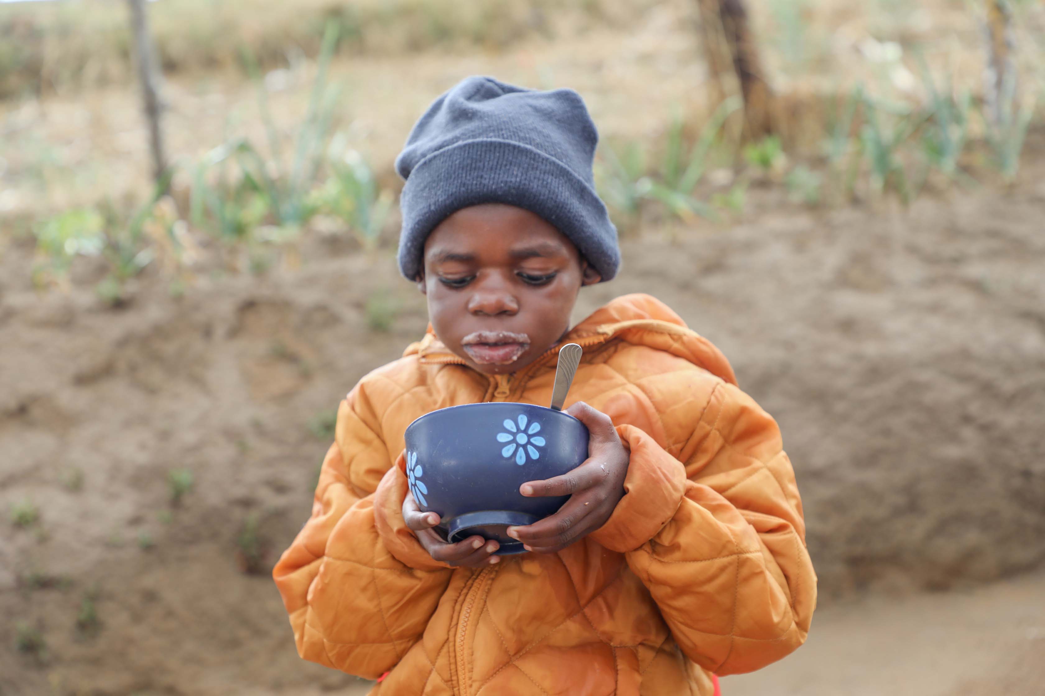 A young boy is looking at the bowl of porridge he's holding