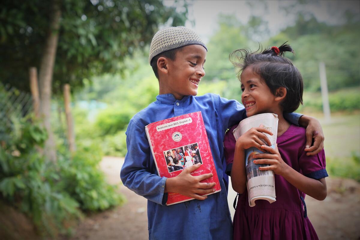 Two children in Bangladesh smile at each other as they hold a book each