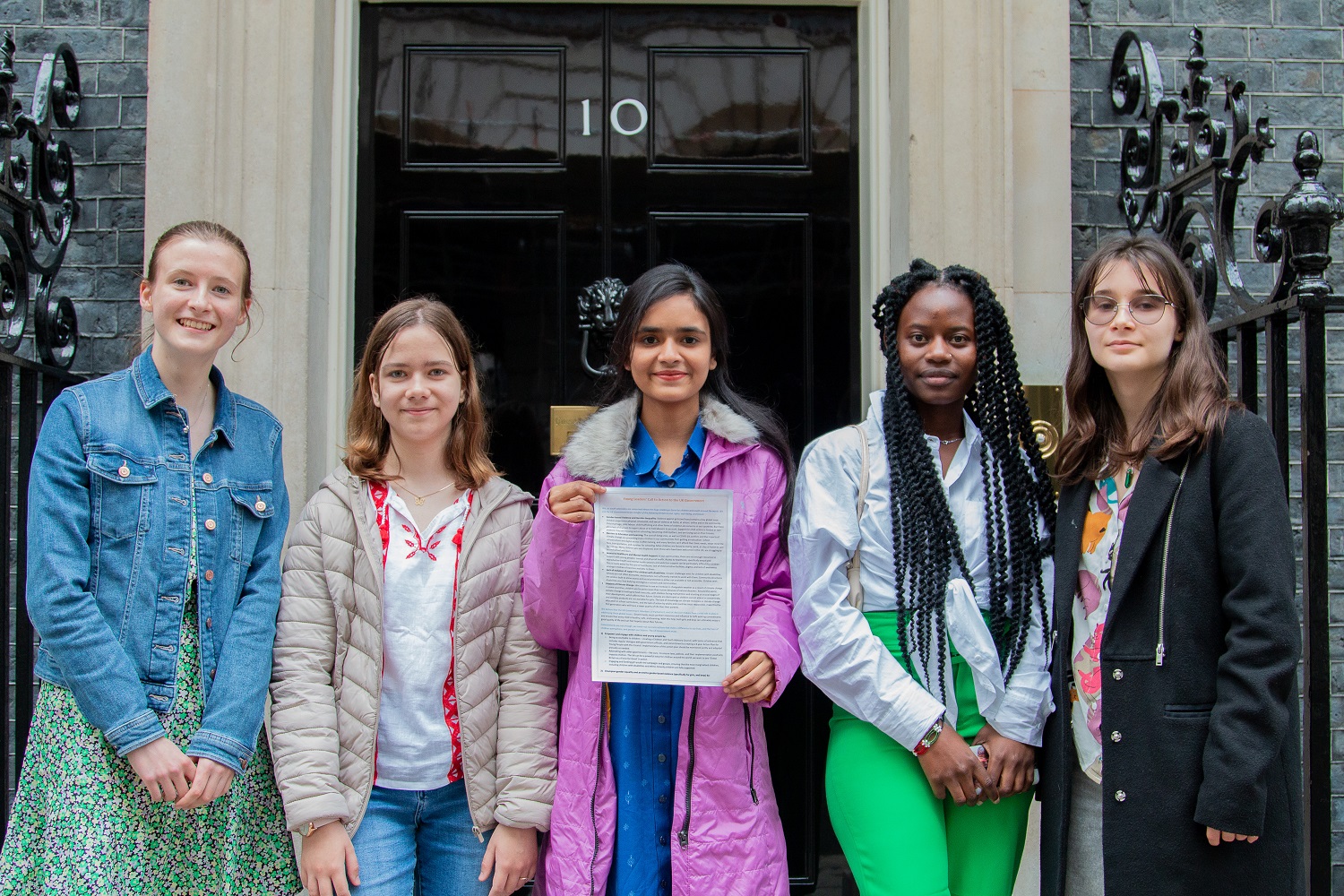 Five young people from Bangladesh, Kenya, Ukraine and the UK stand outside the door to 10 Downing Street, London
