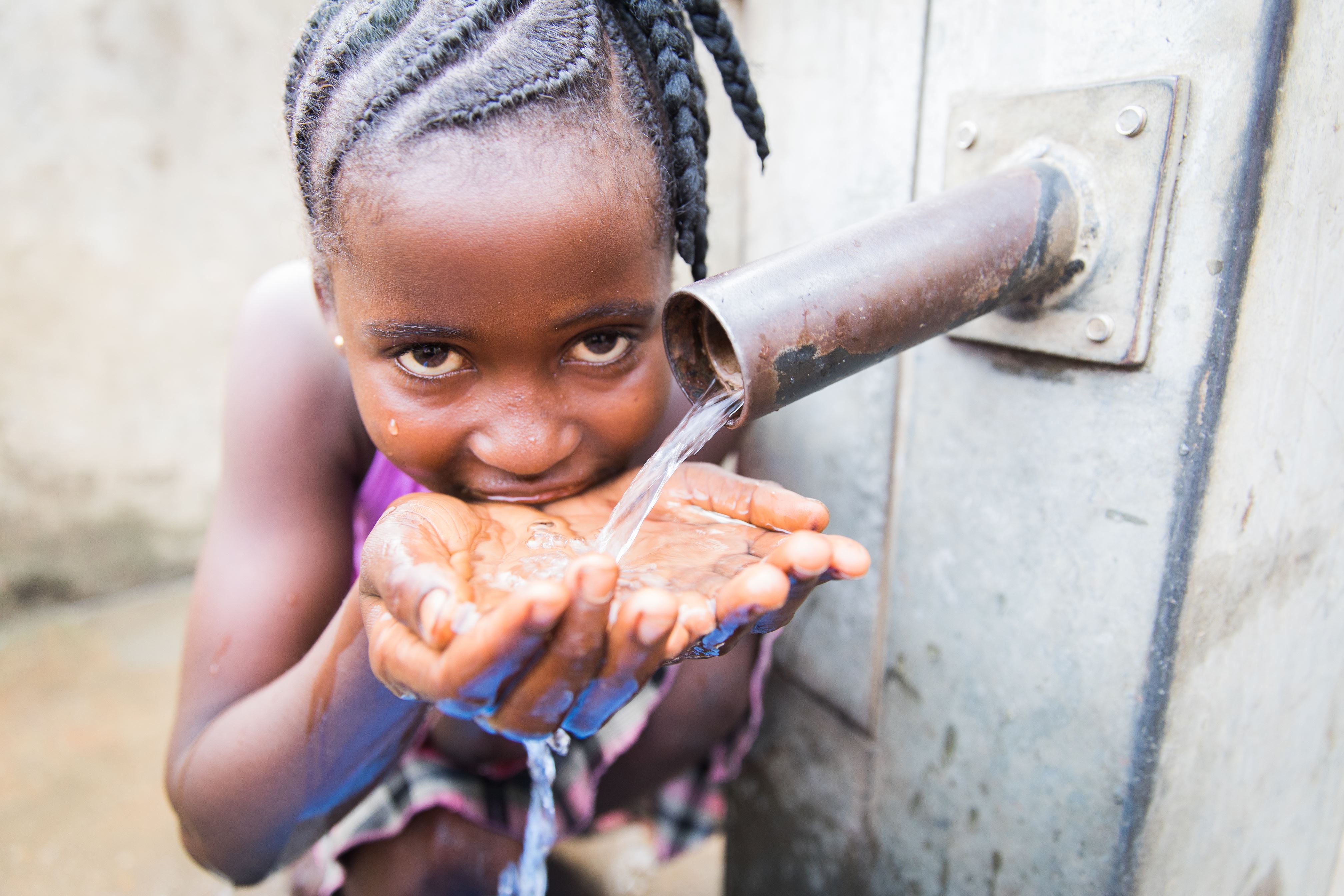 Girl in Sierra Leone holds out her hands to catch clean water from a tap, drinking it