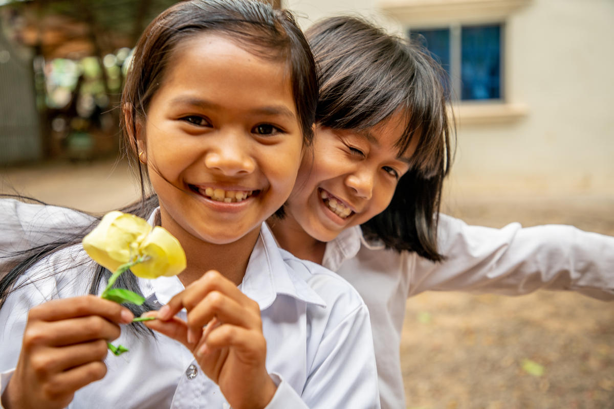 Two girls in Cambodia, wearing school uniform hold flowers