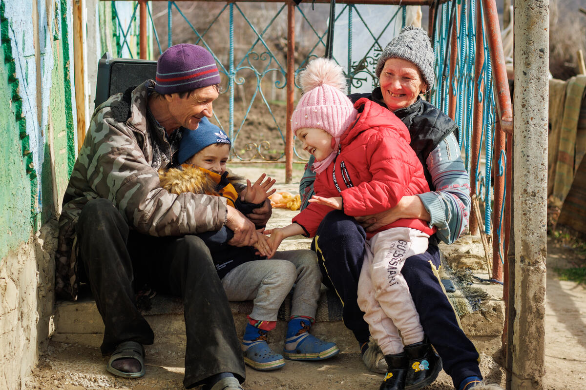 Refugee family sat on a step outside in Moldova. Two children are smiling and playing