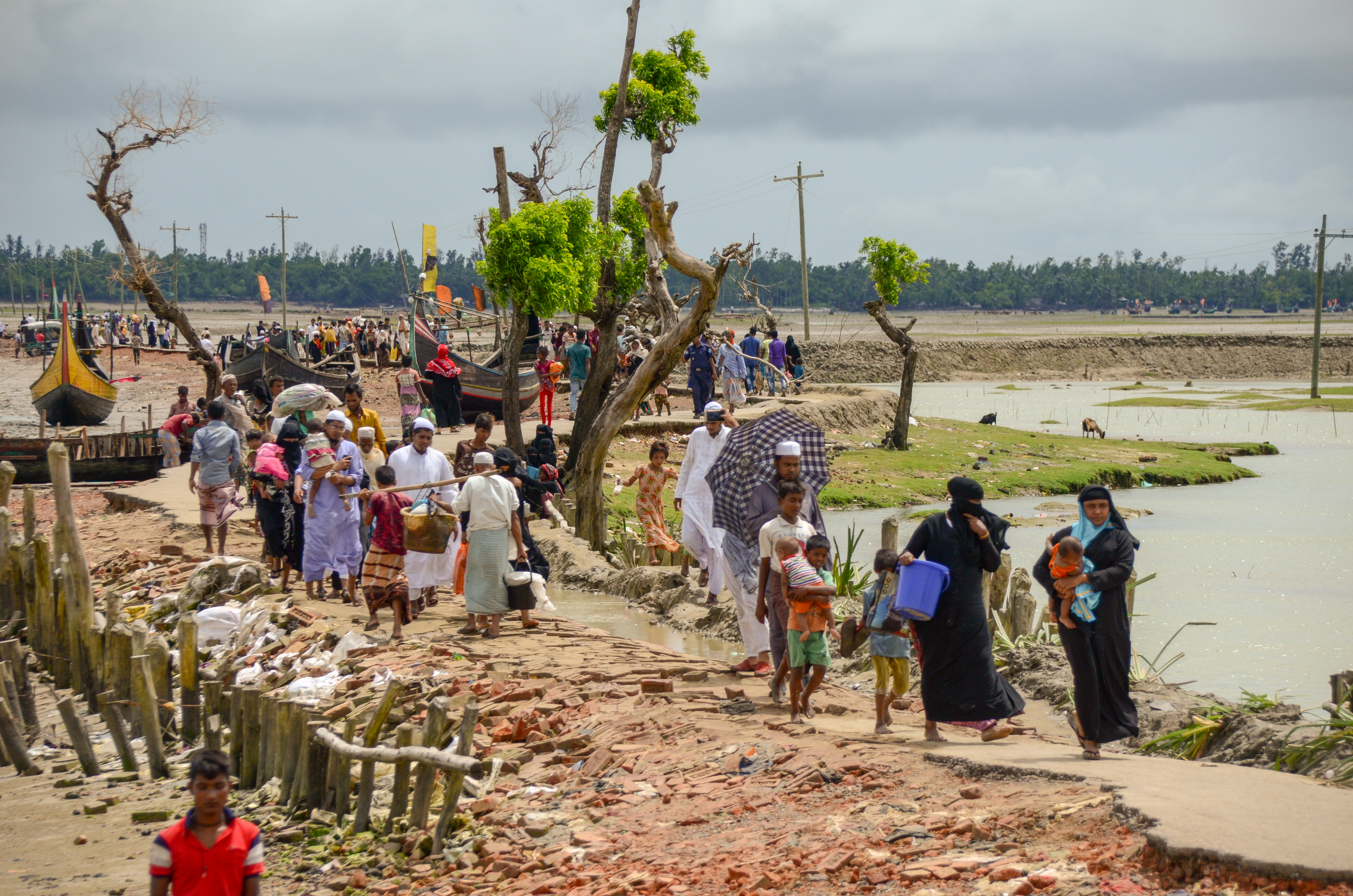 A long line of Rohingya refugees fleeing, carrying small amounts of personal posessions.
