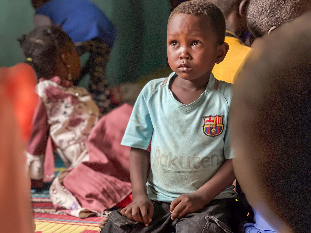 A young boy sits on a mat, there are other children in the background