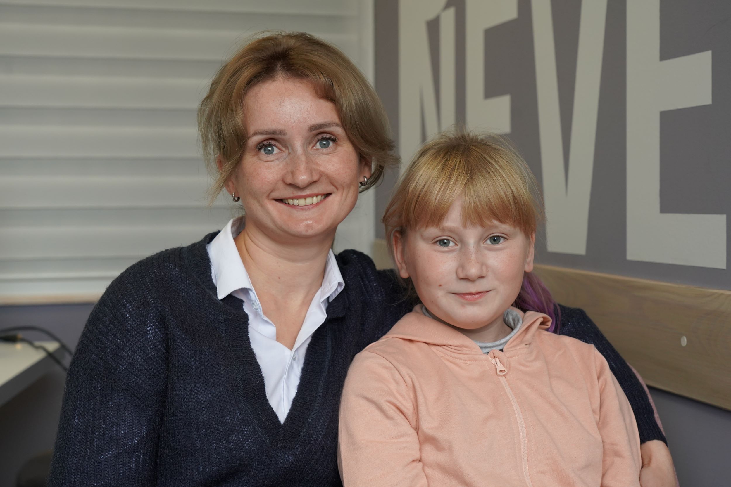 Ukrainian woman in dark blue cardigan sits with her arm around her daughter
