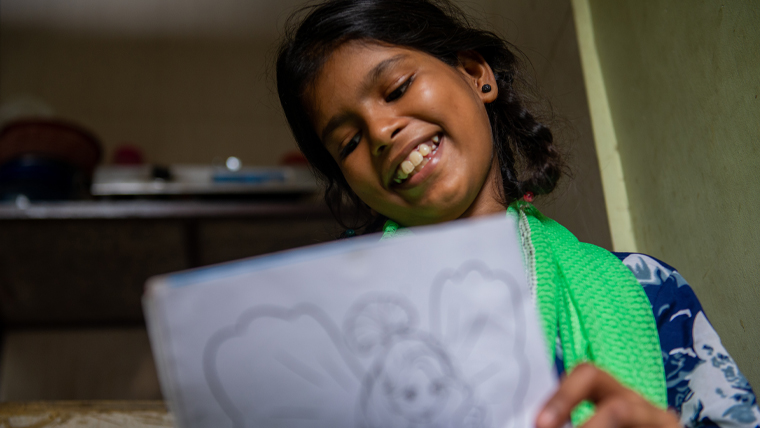 Archana has a huge smile as she enjoys colouring in a picture
