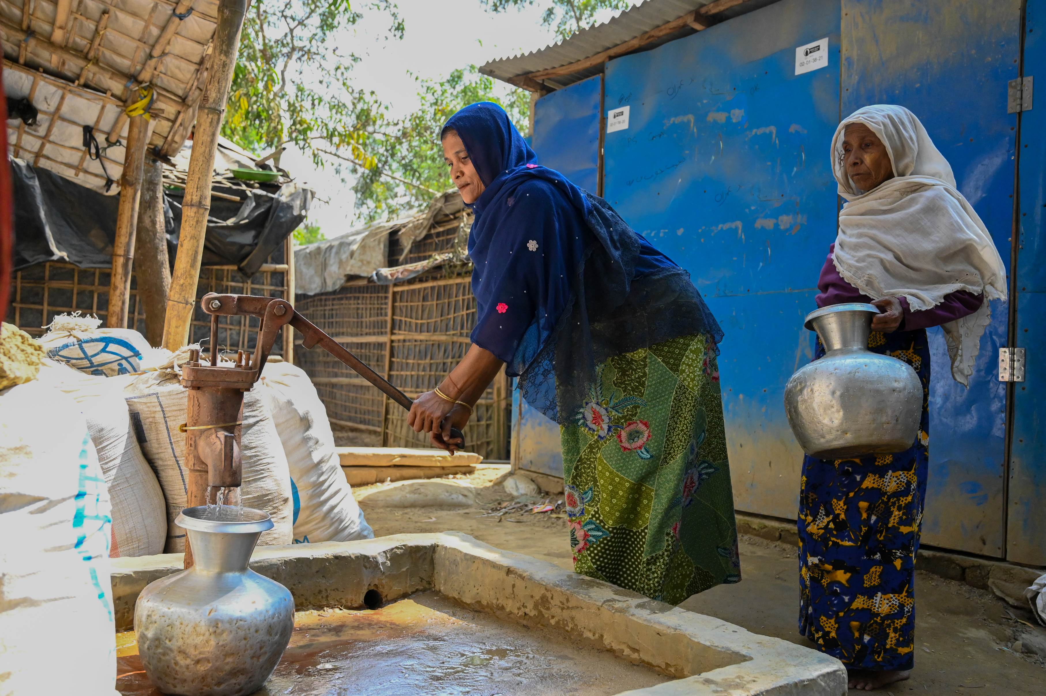 One woman pumps water from a tap while another waits in a refugee camp in Bangladesh