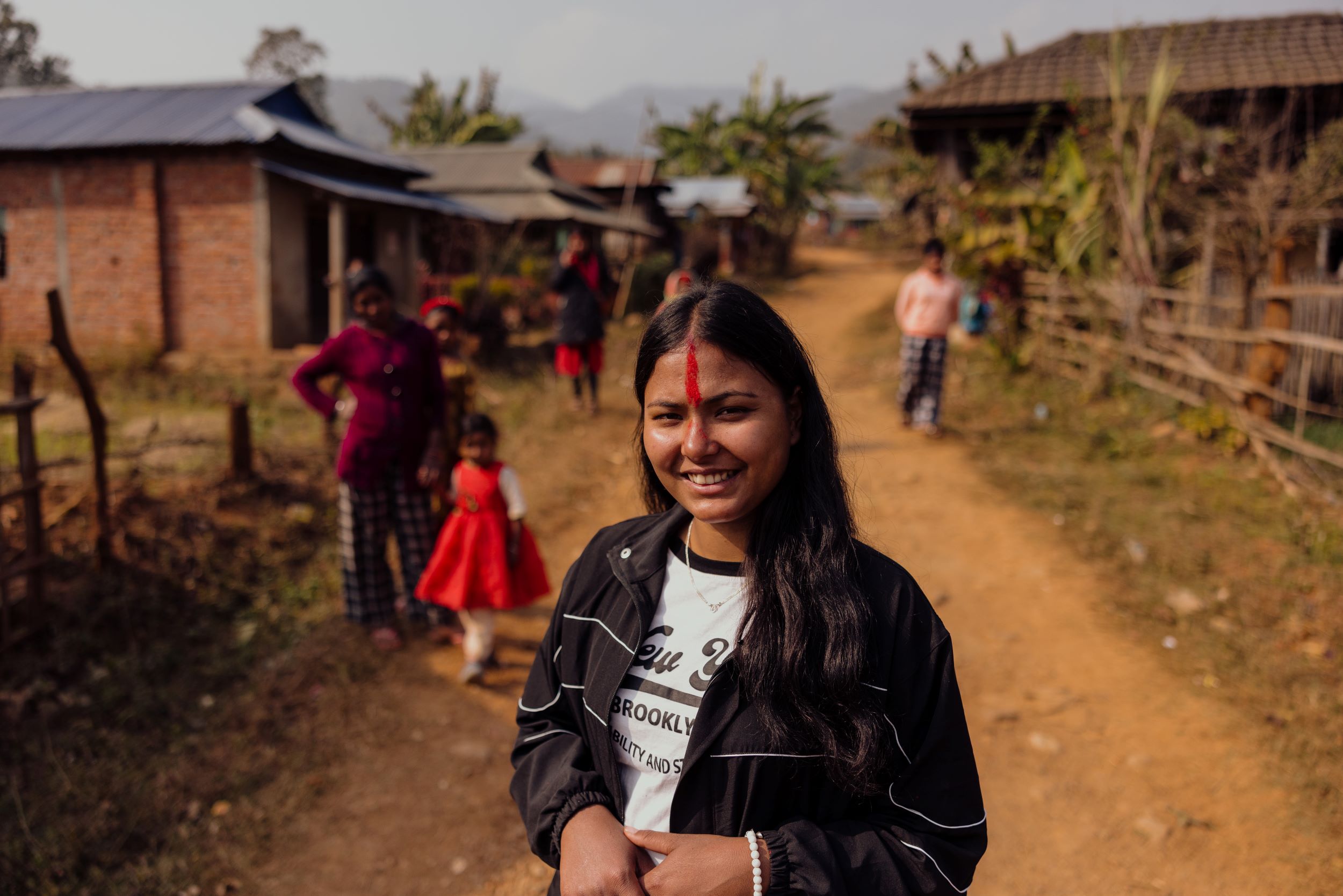 Januka stands before members of her community, a line of traditional red paint down her forehead