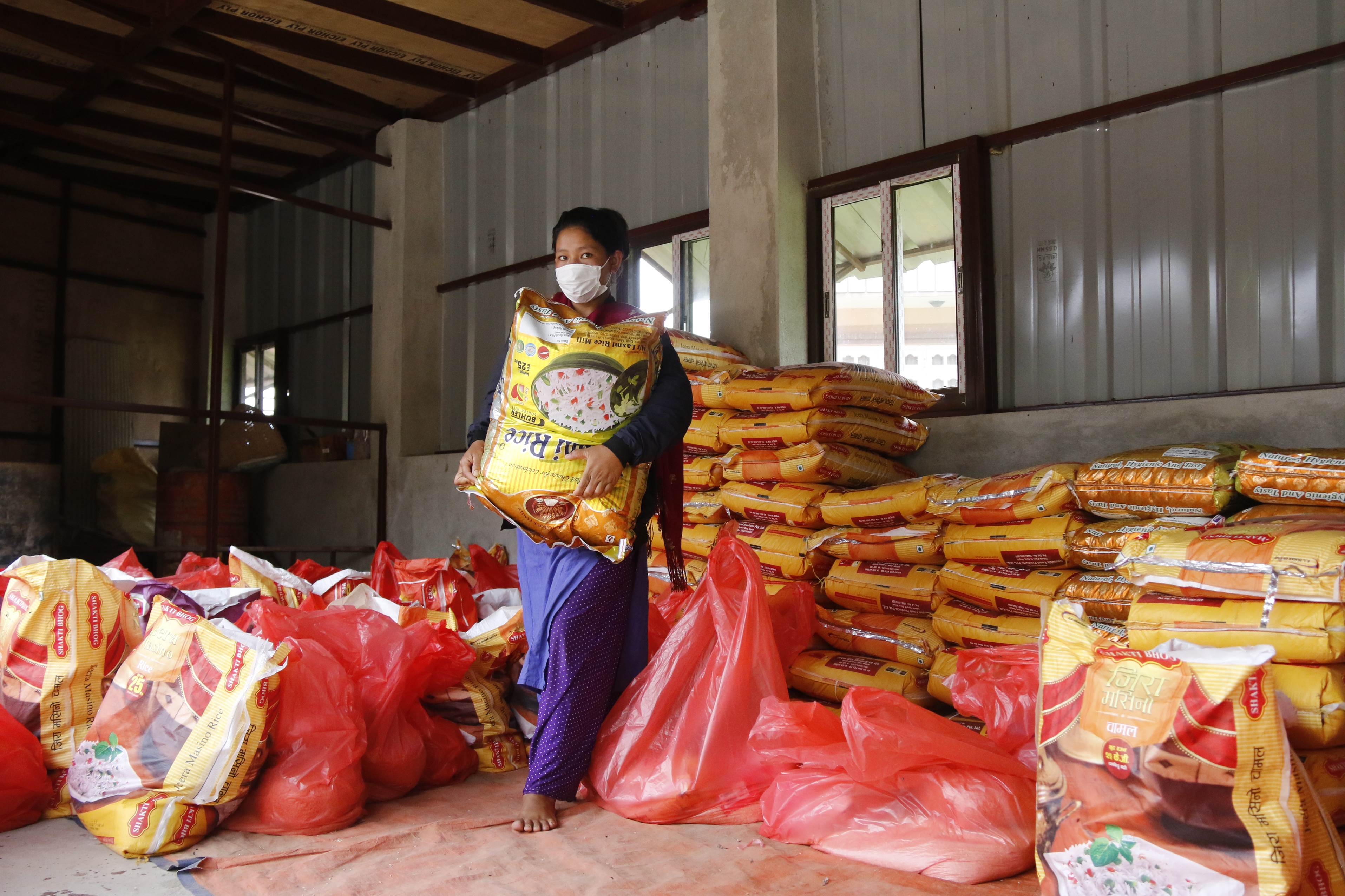 A person carrying a food pack in a warehouse in Nepal with lots of food packs piled up around them