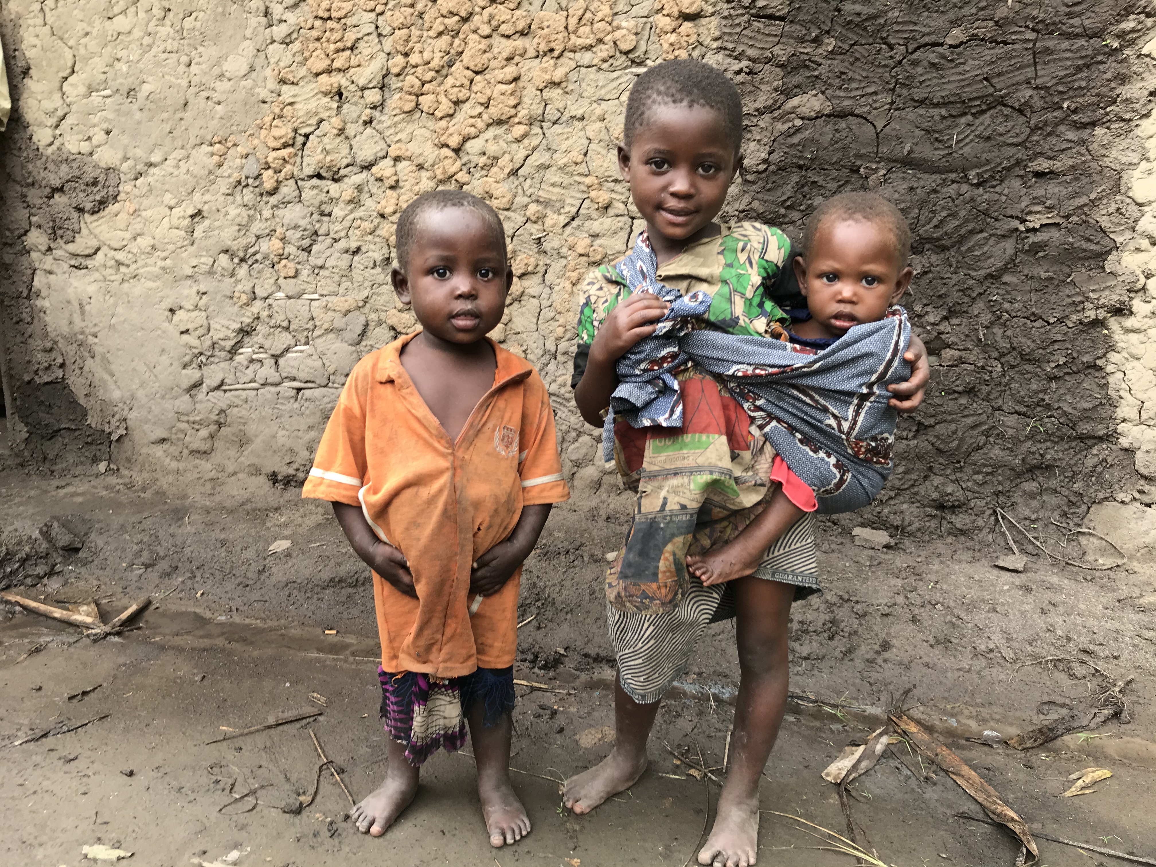 Two young children, one of them holding a third very young child, standing outside
