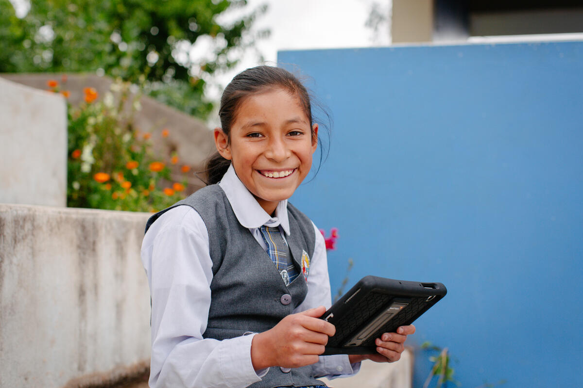 A young girl smiles at the camera whilst holding a tablet