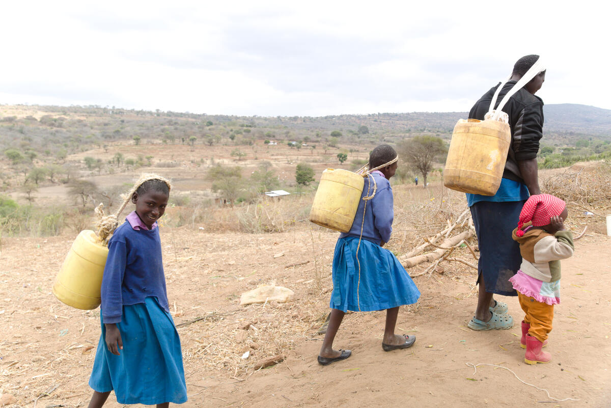 A woman and her three daughters walk with large containers to collect water during drought