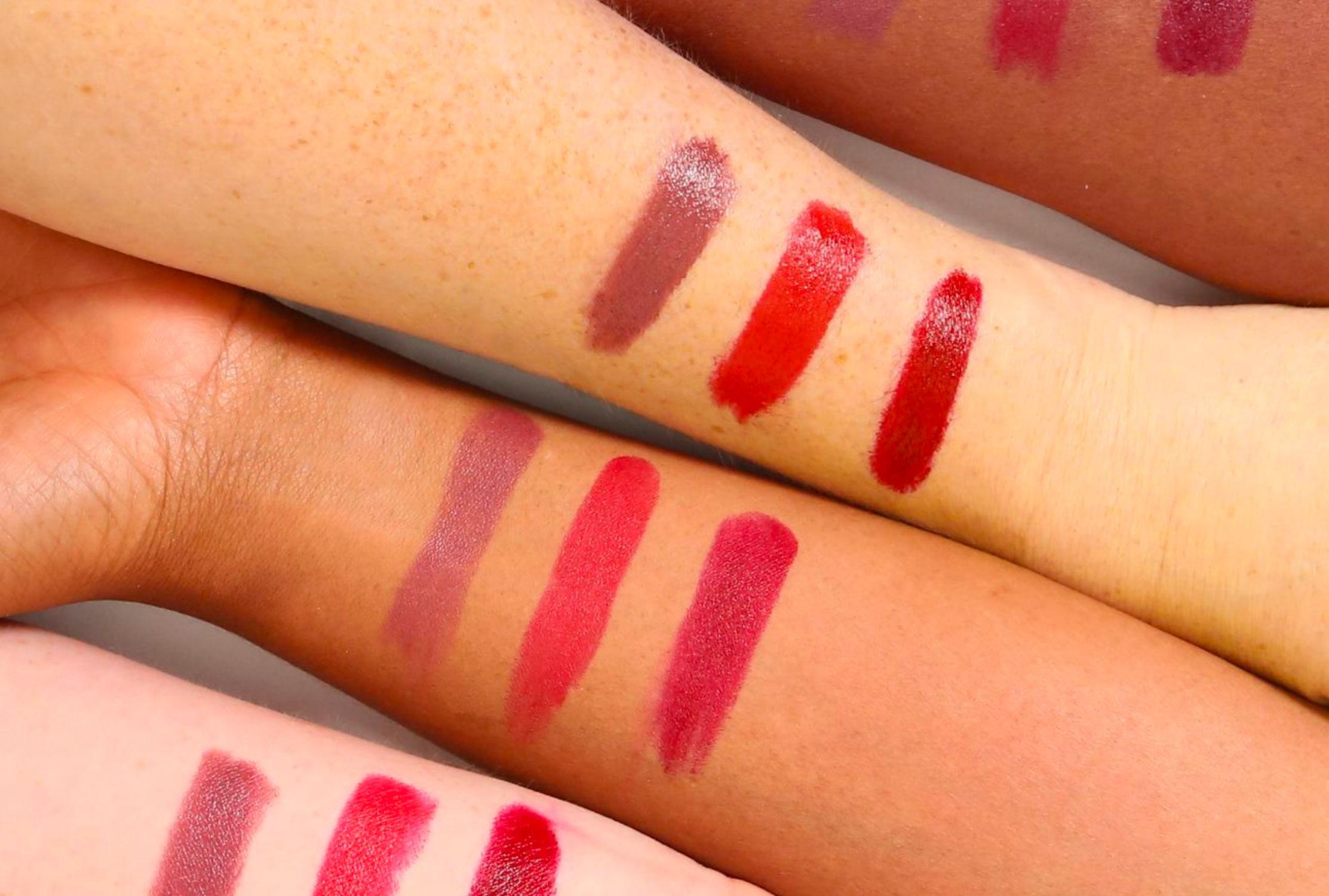 Different lipstick shade swatches on four arms of varying skin tones