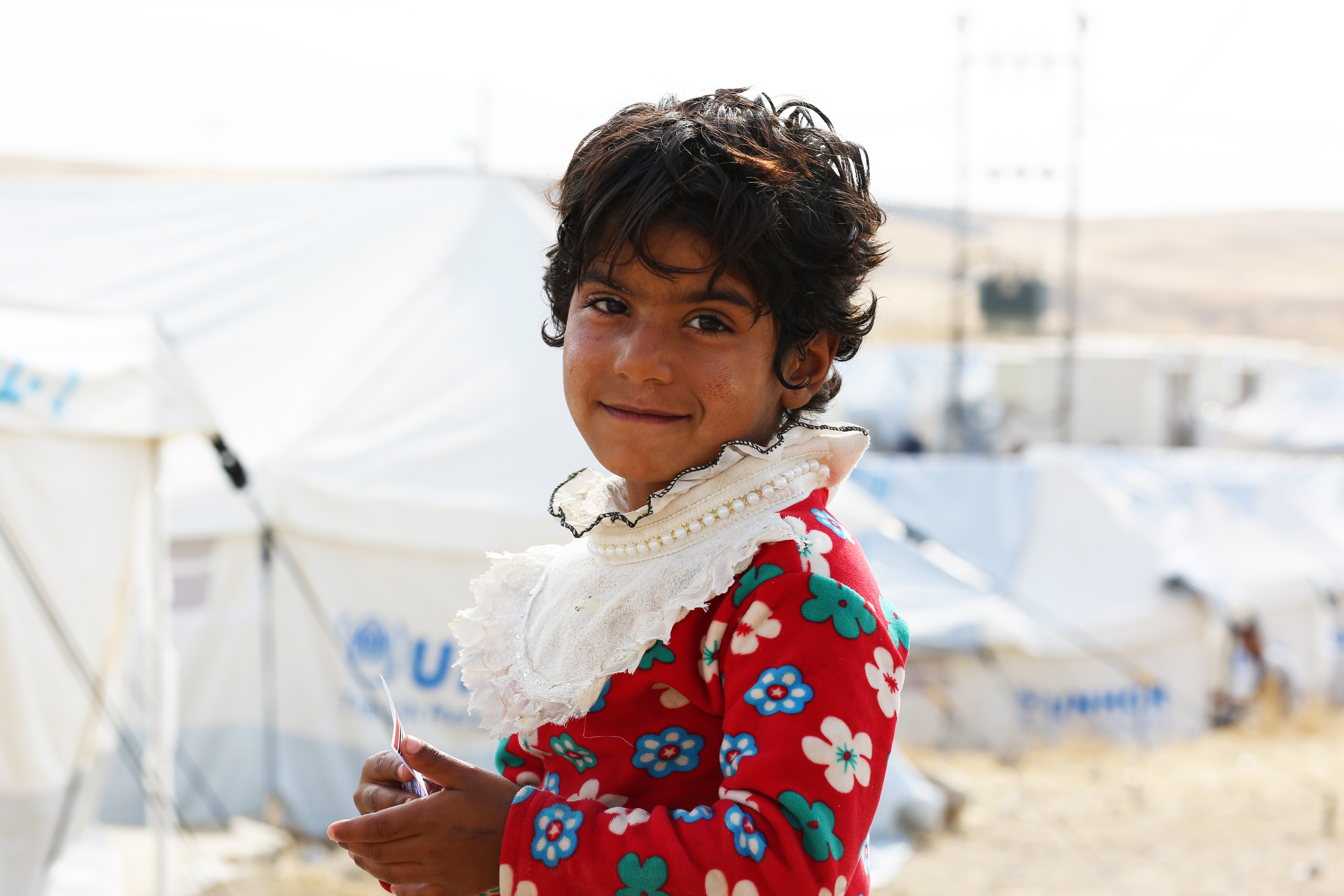 Young child staring into camera with tents in the background