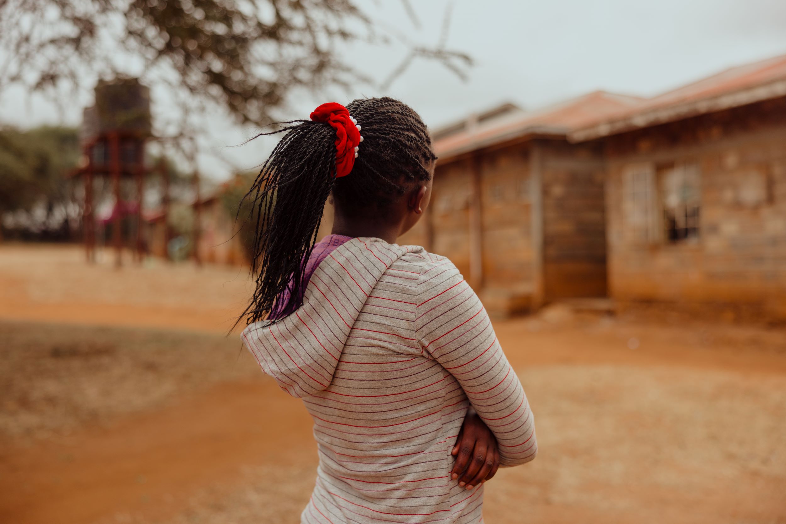 Kenyan girl with ponytail and long-sleeved hoody, looking towards building.