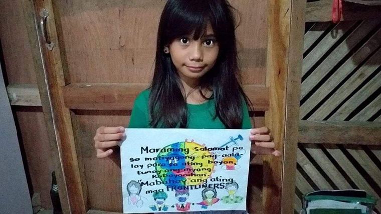 Girl from the Phillipines holds up a drawing she has done to thank health workers