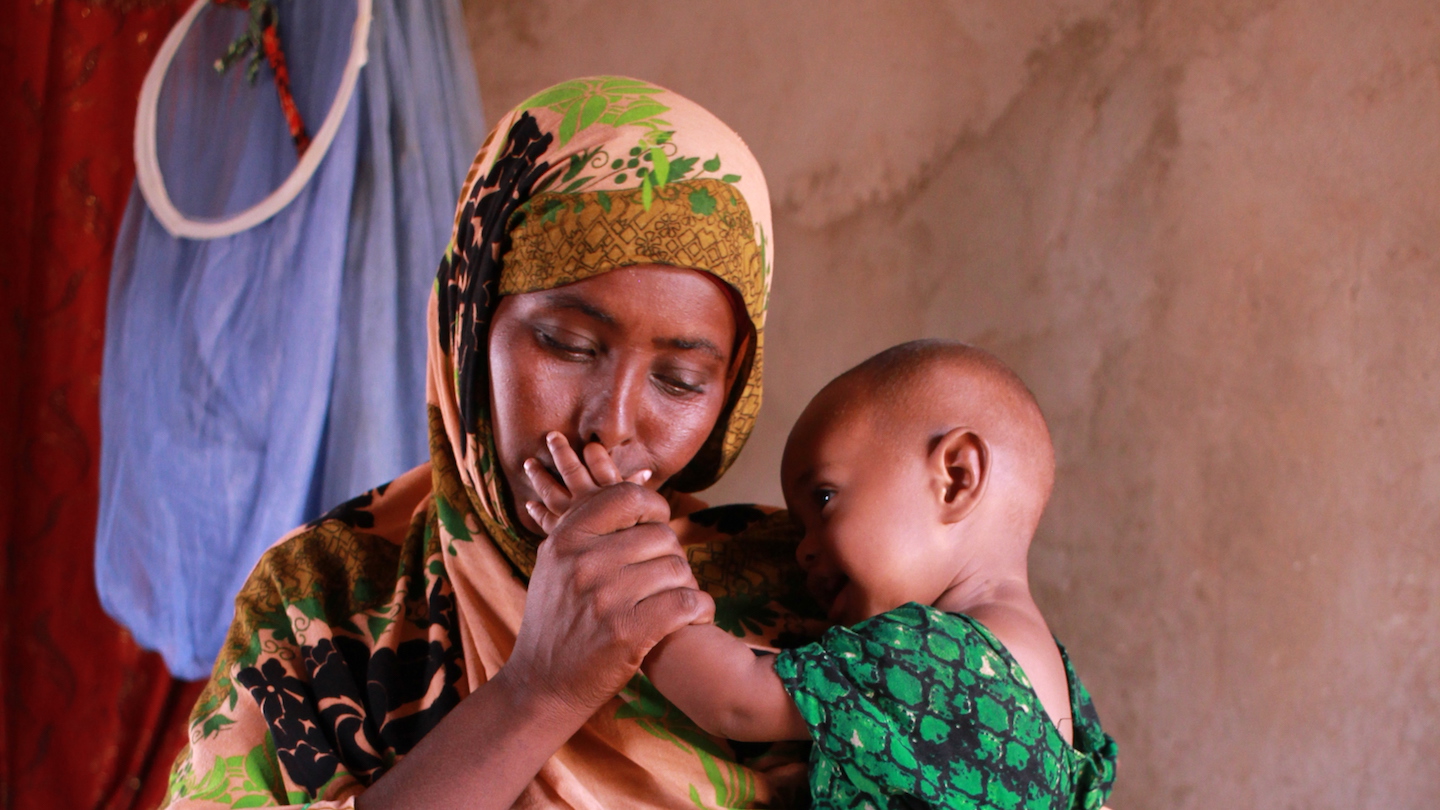 A mother holds her little baby and kisses its hand
