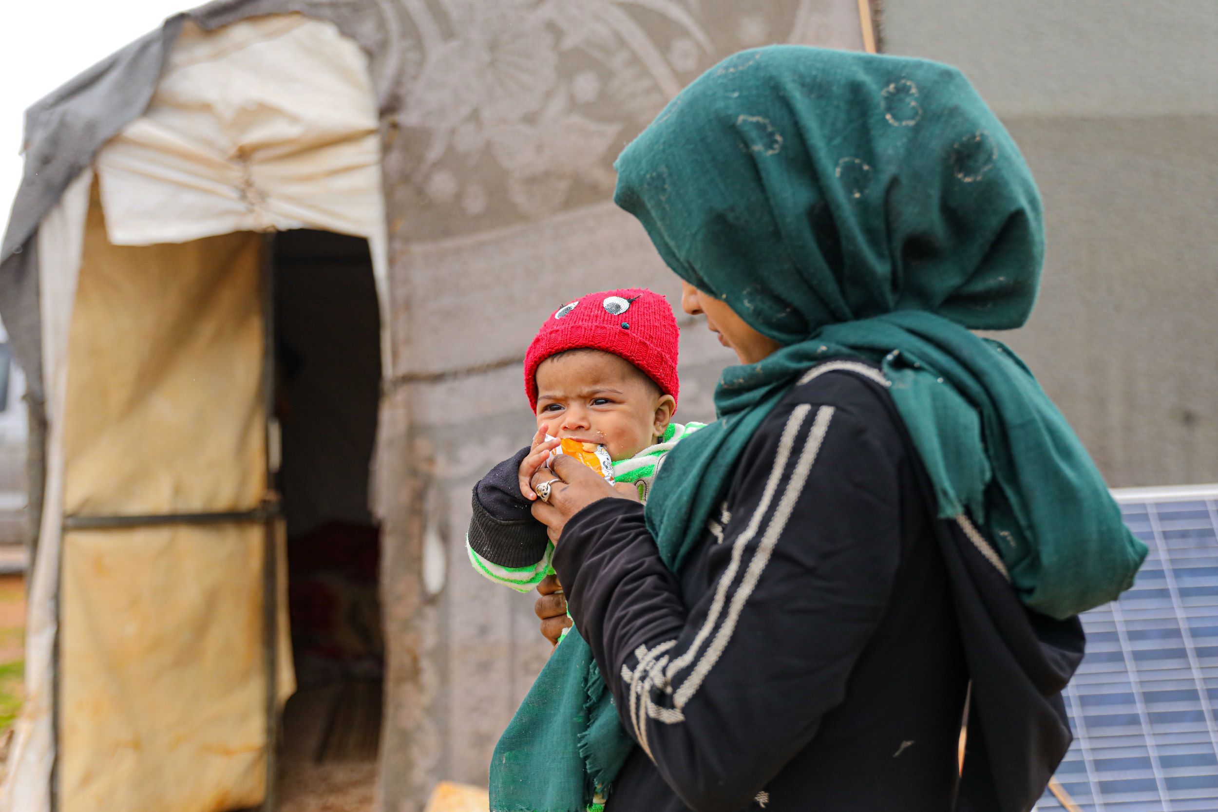 Baby in red hat held by her mum, being fed nutritional supplements that treat child malnutrition