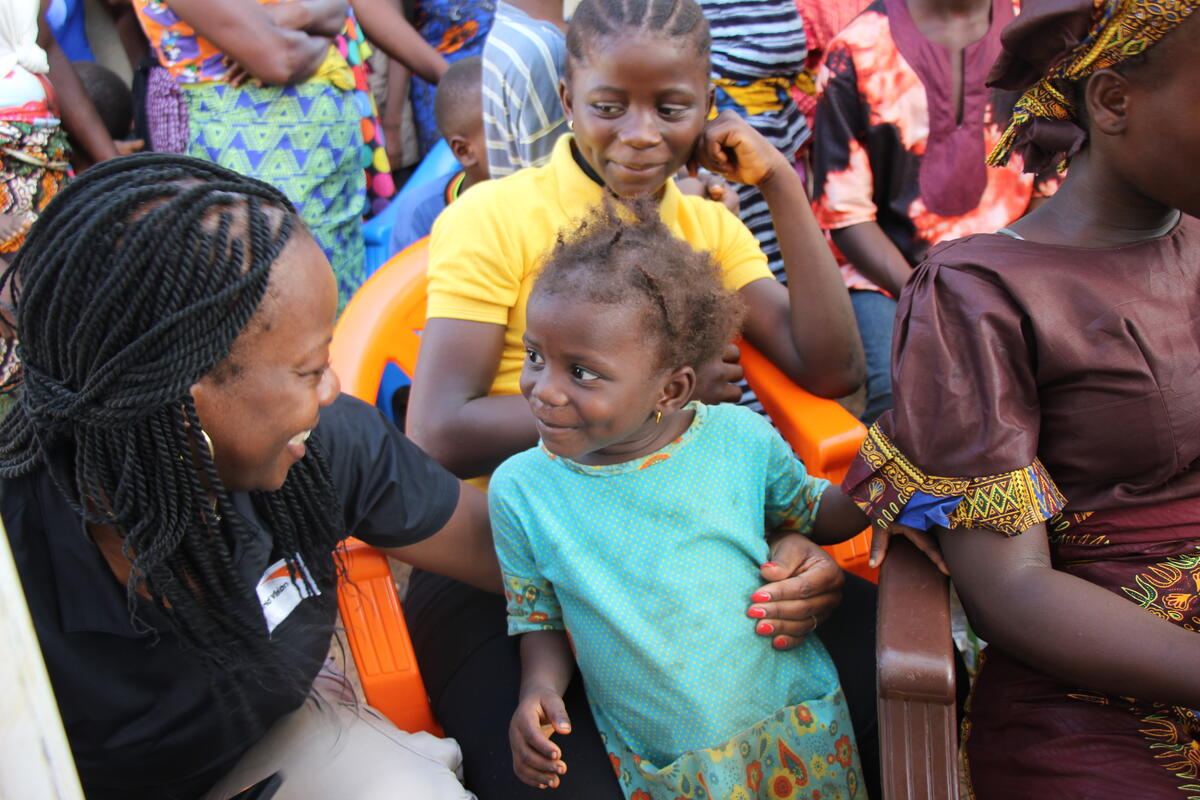 Child from Sierra Leone looking at World Vision staff member and smiling, amongst a crowd of others