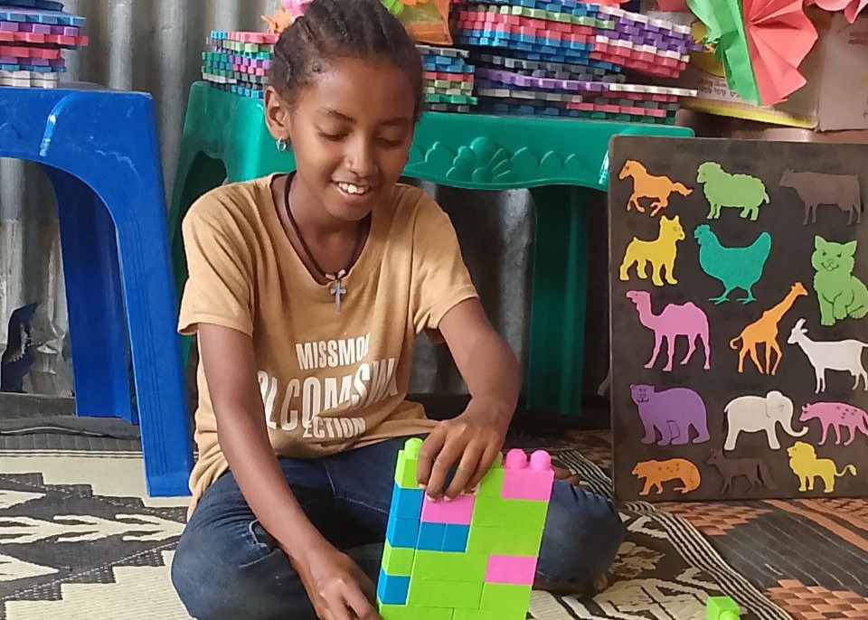 Tsion, 9, smiles as she sits and plays with colourful bricks at a Child Friendly Space in Ethiopia