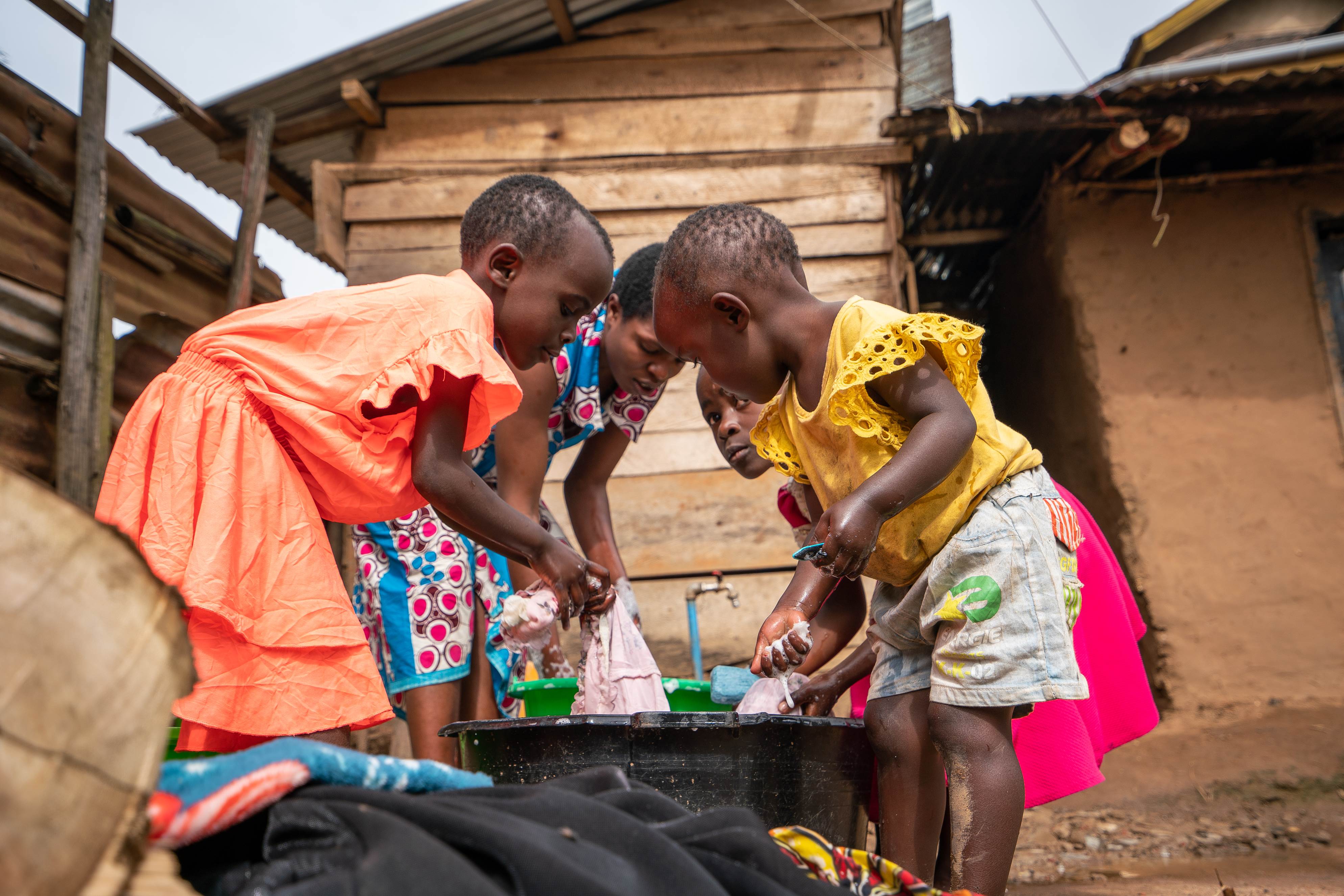 Four people in DRC wash their clothes outdoors in a large black pot