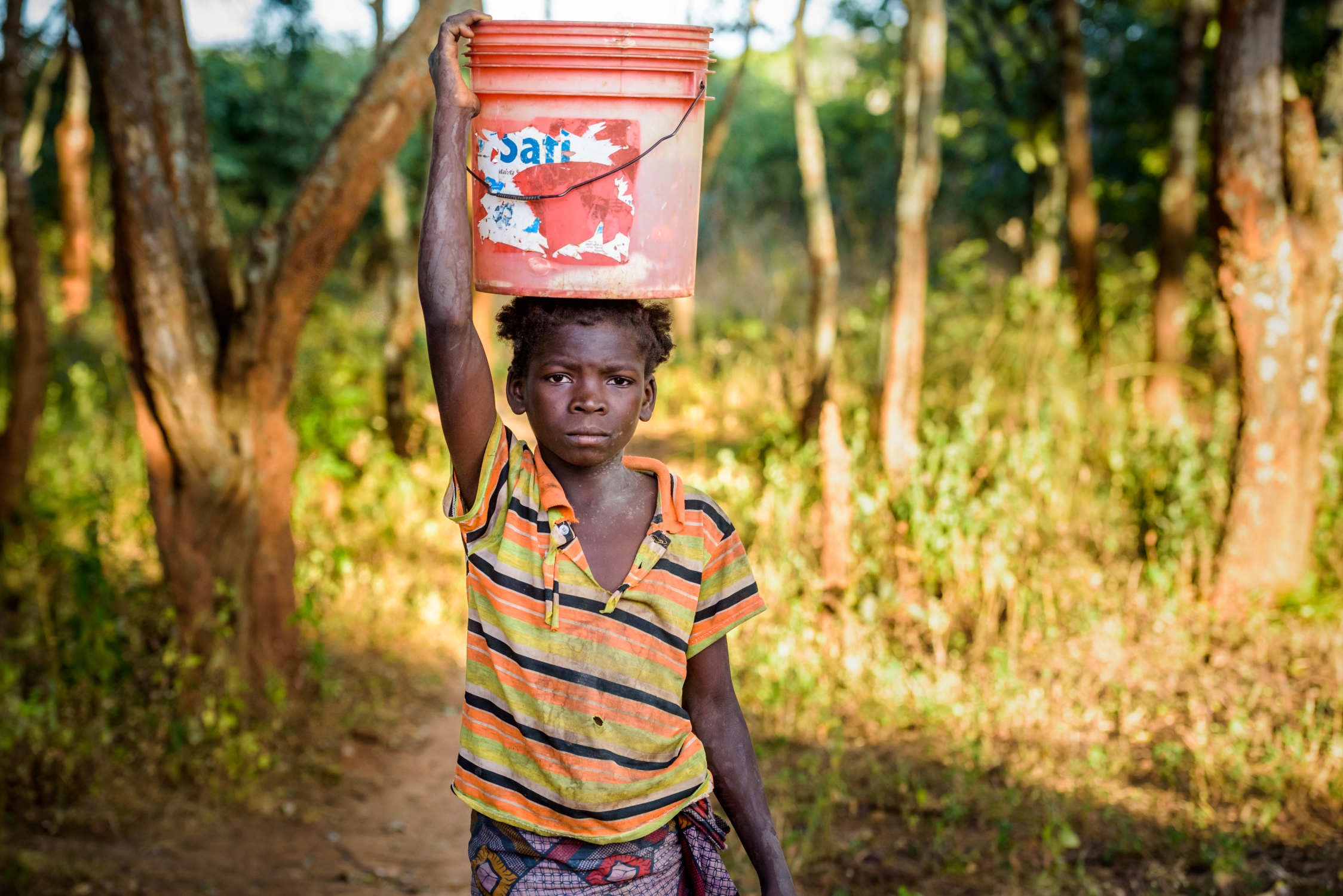 Ruth carries water home in a large bucket balanced on her head.