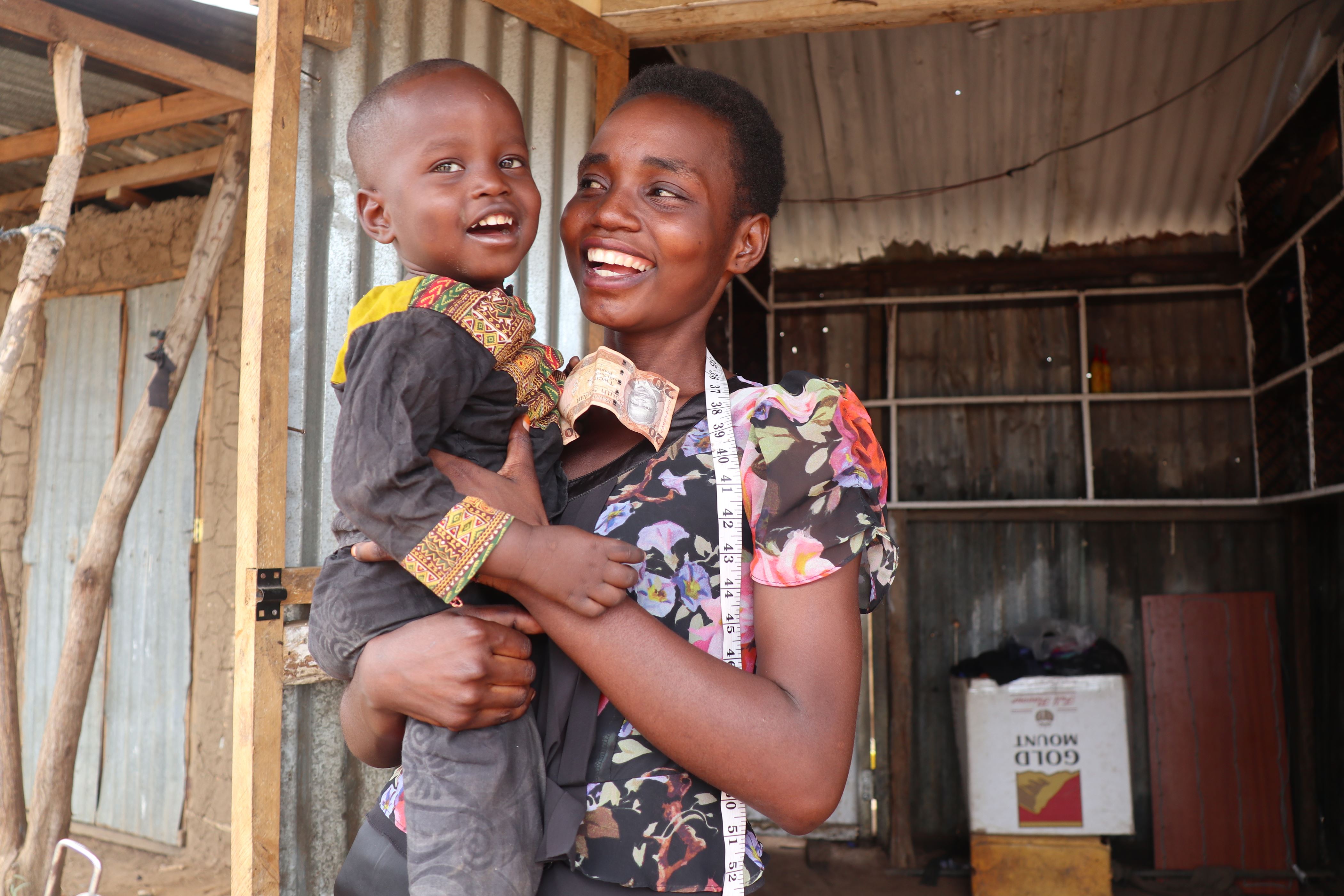 Woman holds her son in her arms and smiles at him, in front of an open door, with a view into the room behind in South Sudan